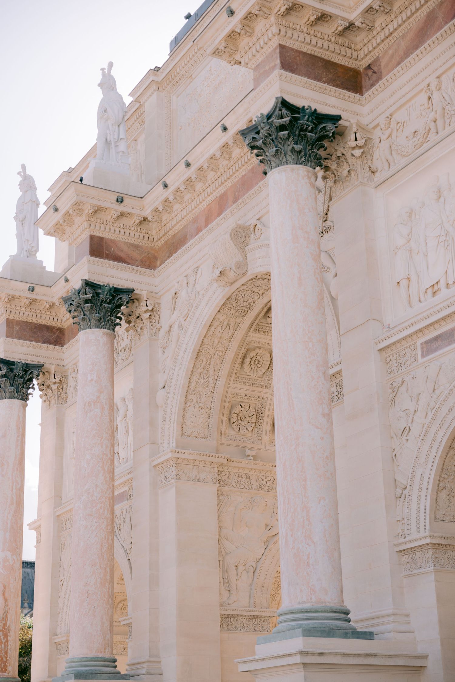 Classical colonnade with white stone pillars and decorative Corinthian capitals against pale sky.