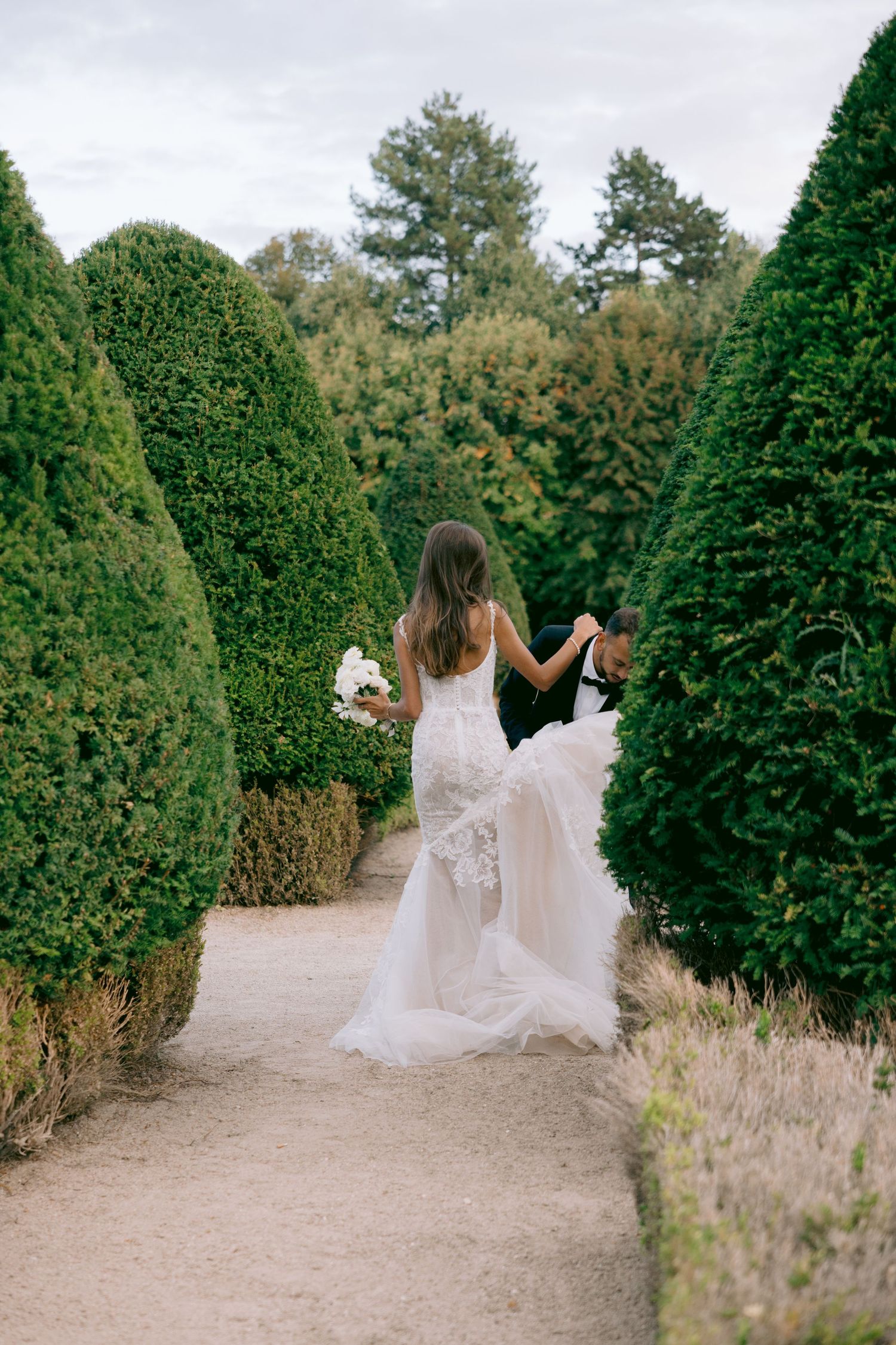 A romantic garden path lined with tall manicured hedges creates an enchanting wedding photo backdrop.