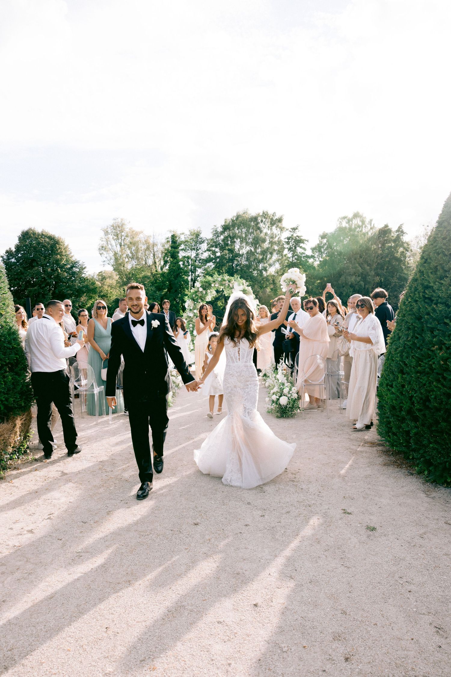 Château de Sept Saulx Wedding party and guests celebrate on a garden path lined with manicured hedges.