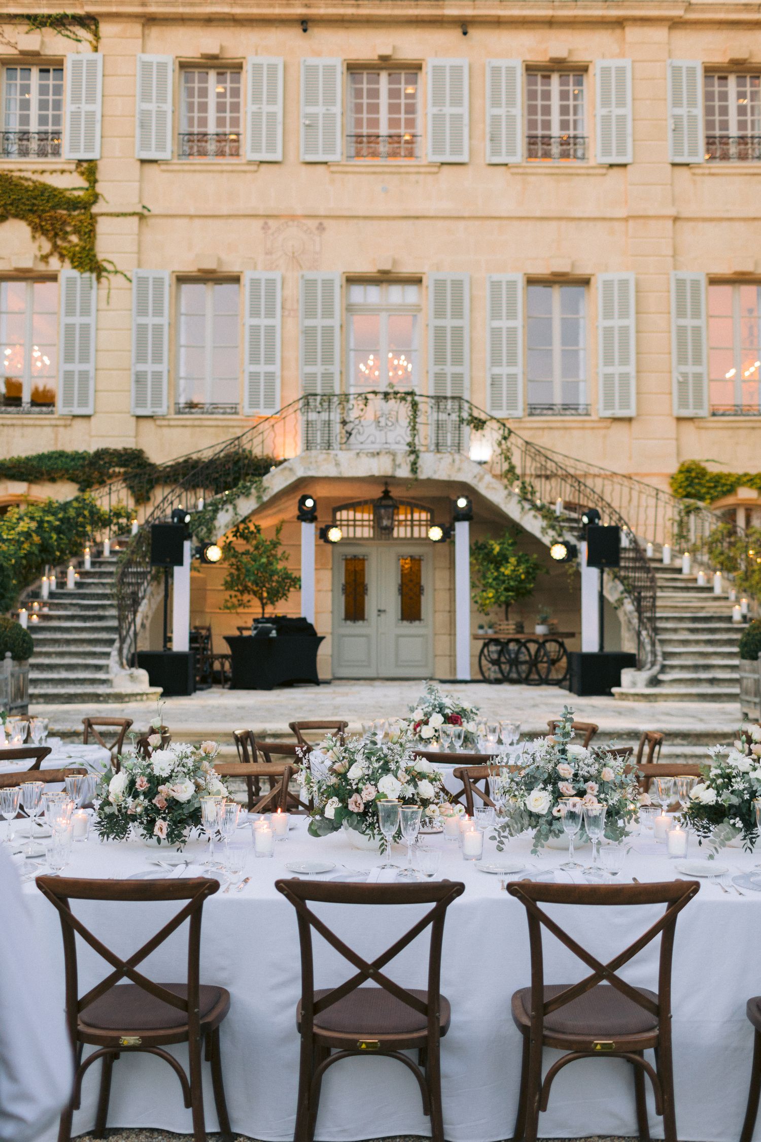 Row of rustic wooden cross-back chairs set up for an outdoor wedding reception against a historic building facade.