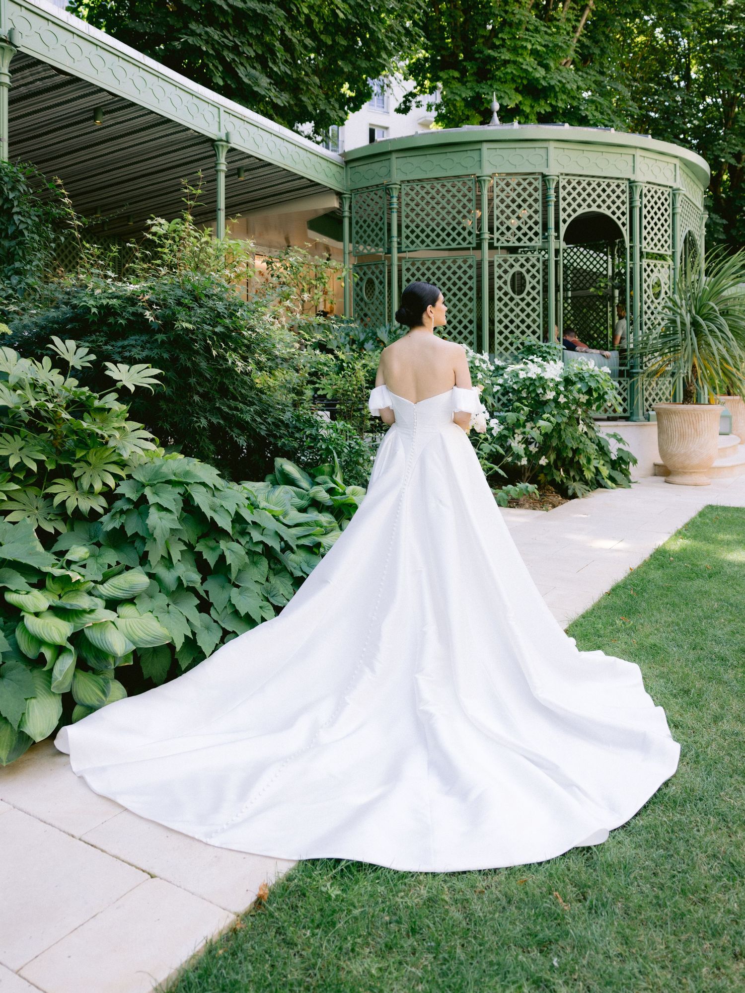 Stunning white wedding gown with dramatic train photographed in front of garden gazebo.