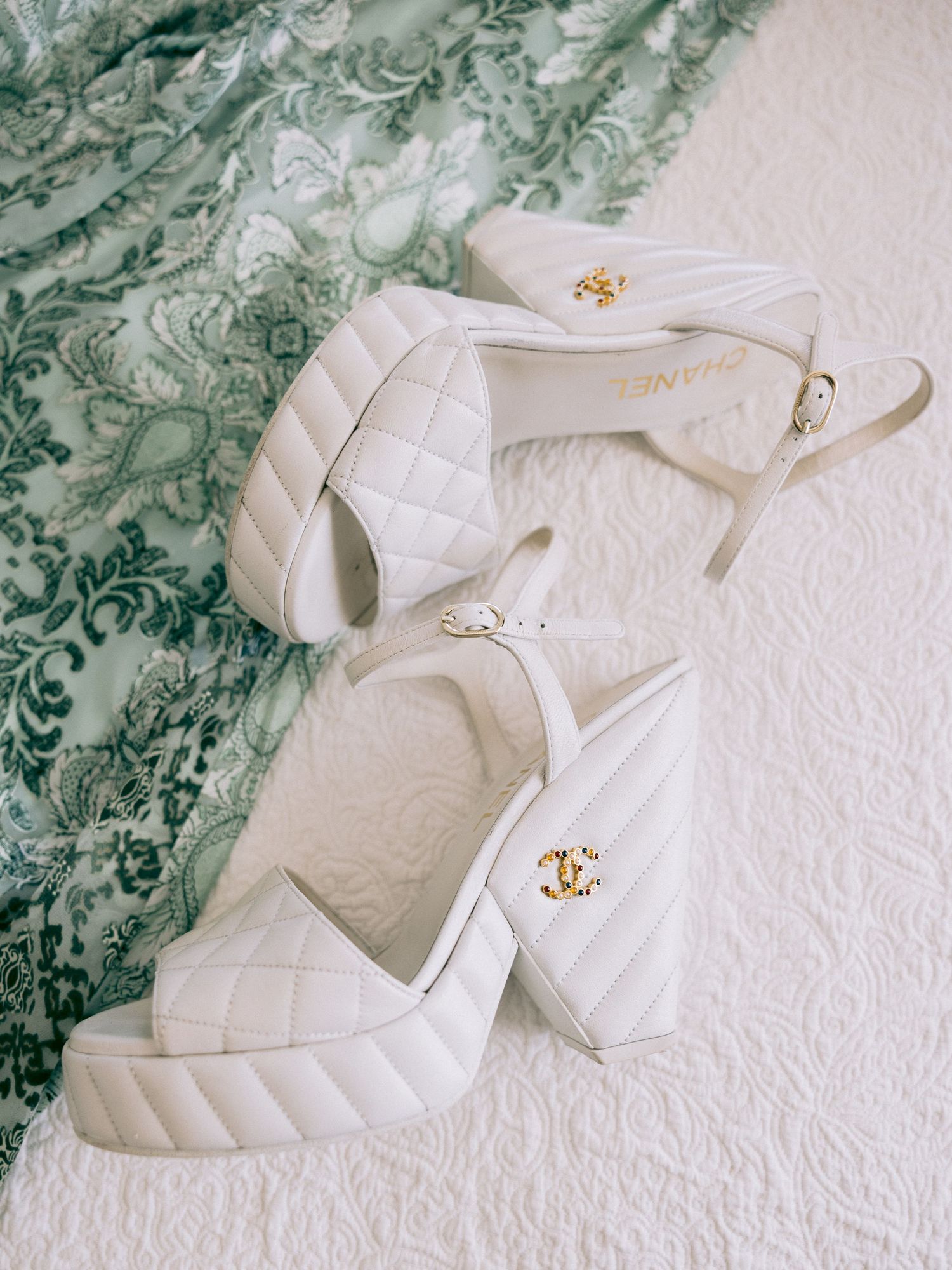 White designer wedding shoes with quilted pattern and gold hardware on textured background.