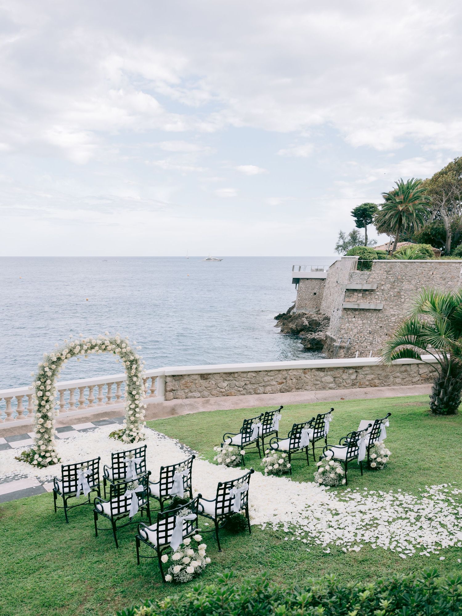 Elegant outdoor wedding ceremony setup with white floral arches and black chairs overlooking the ocean.