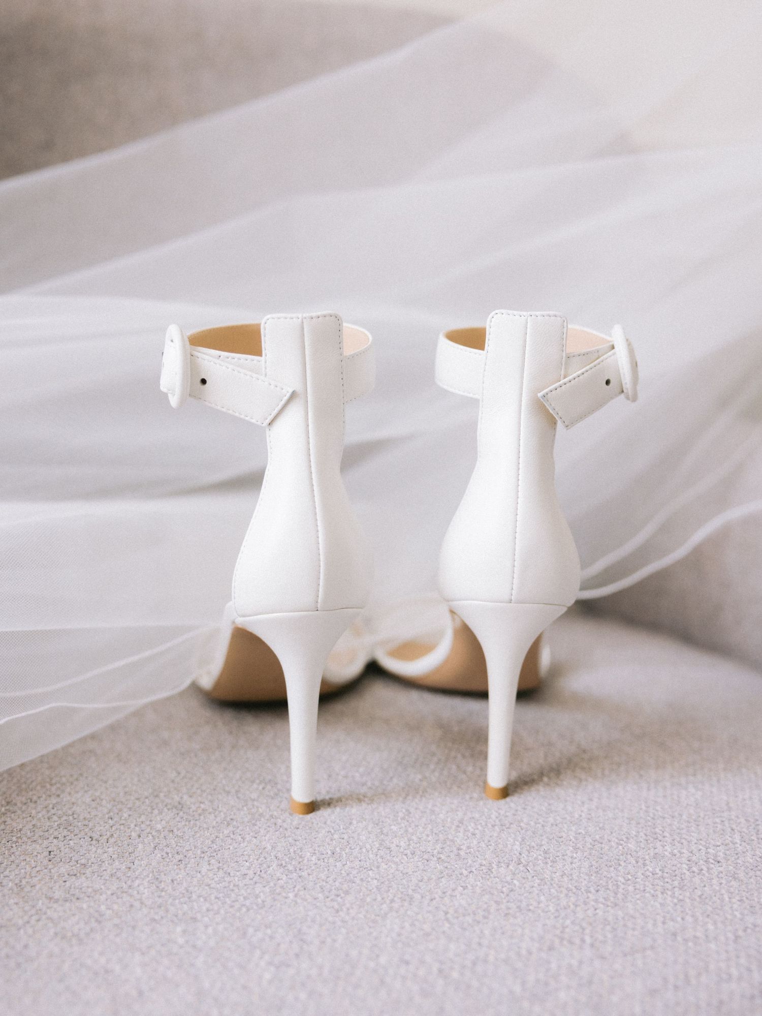 Elegant white bridal shoes with kitten heels photographed on neutral background.