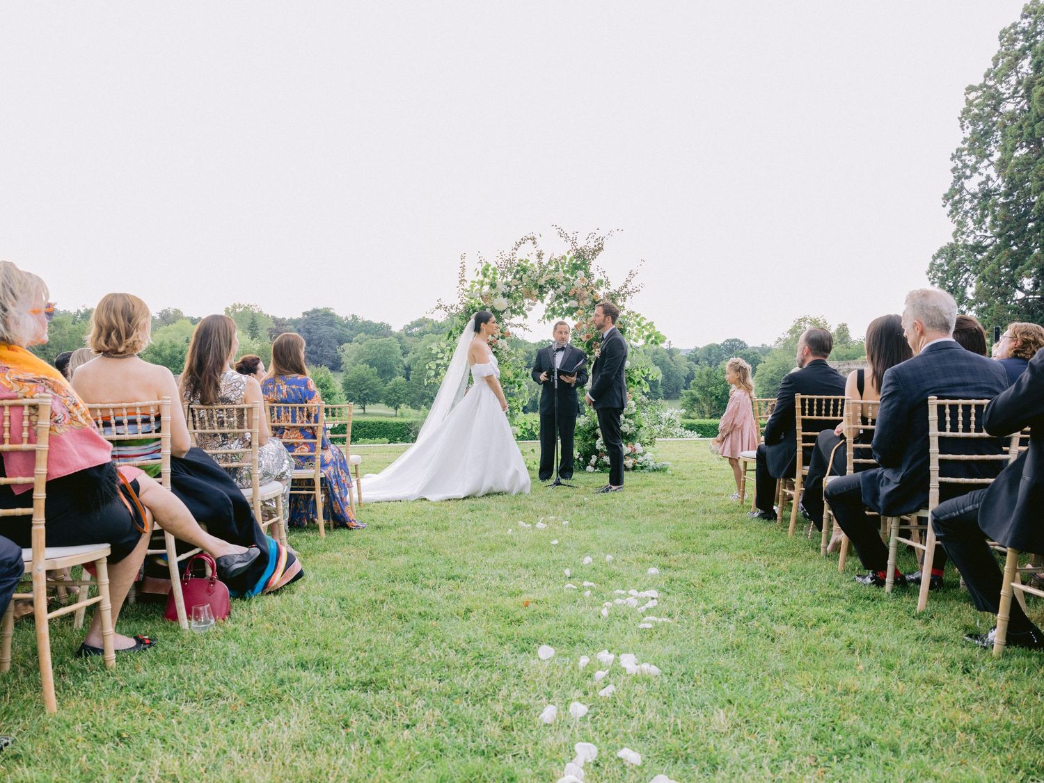 Wedding ceremony setup outdoors with wooden chairs arranged on a grassy lawn.