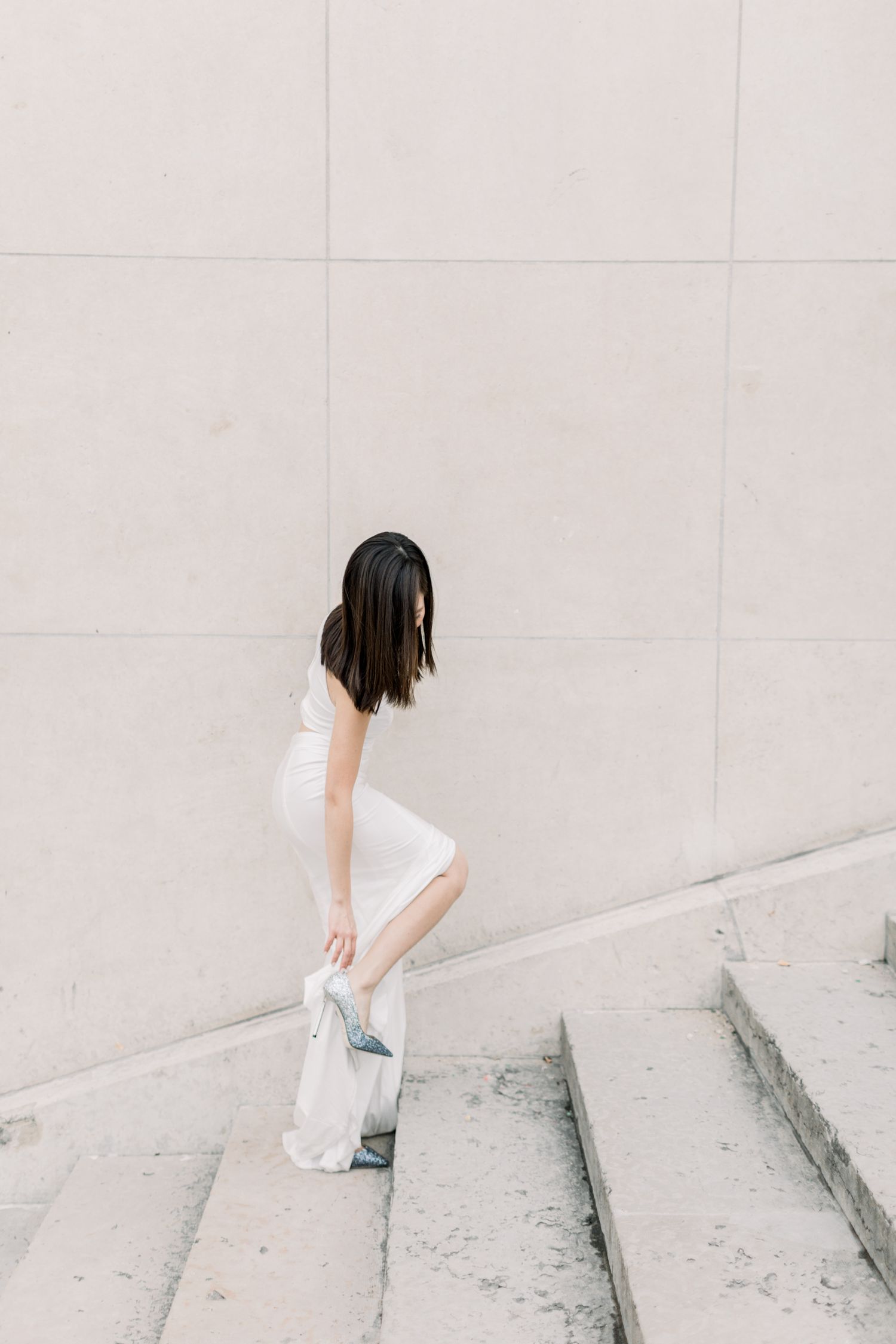 Woman in white dress adjusting her shoe on stone steps.