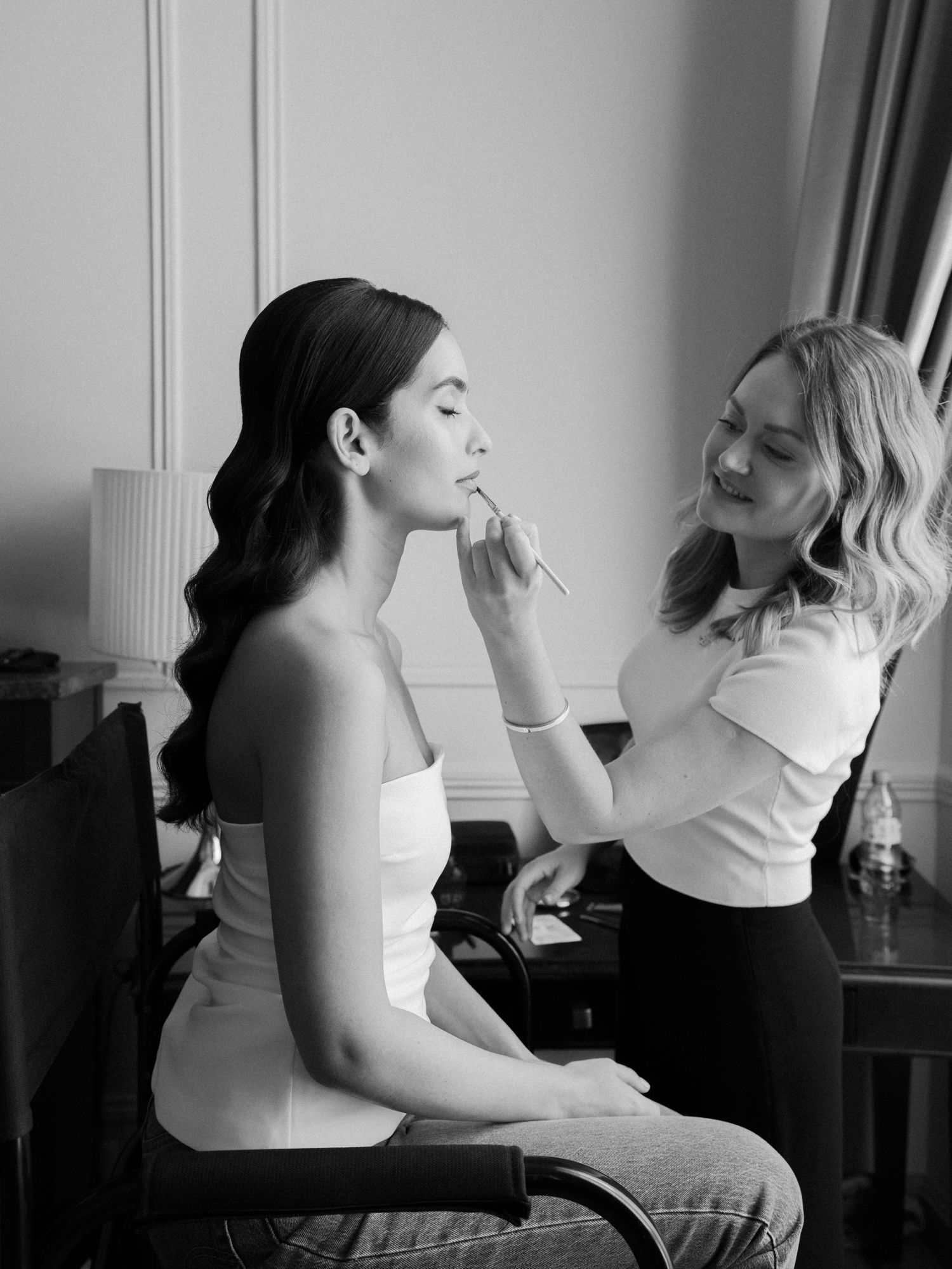 Two people getting ready in formal attire, sitting at a vanity.