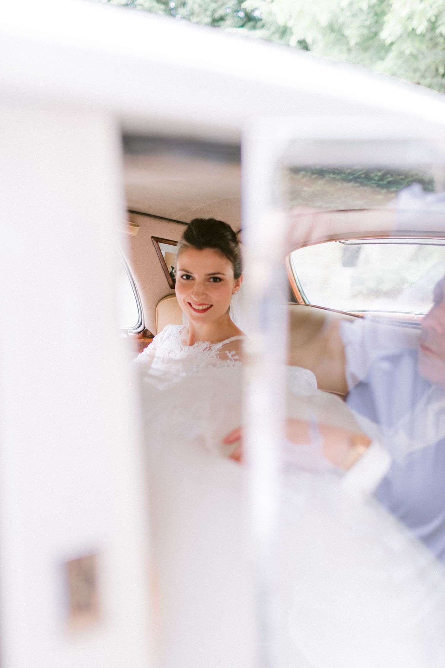 Elegant bride smiling through the window of a classic white vintage car.