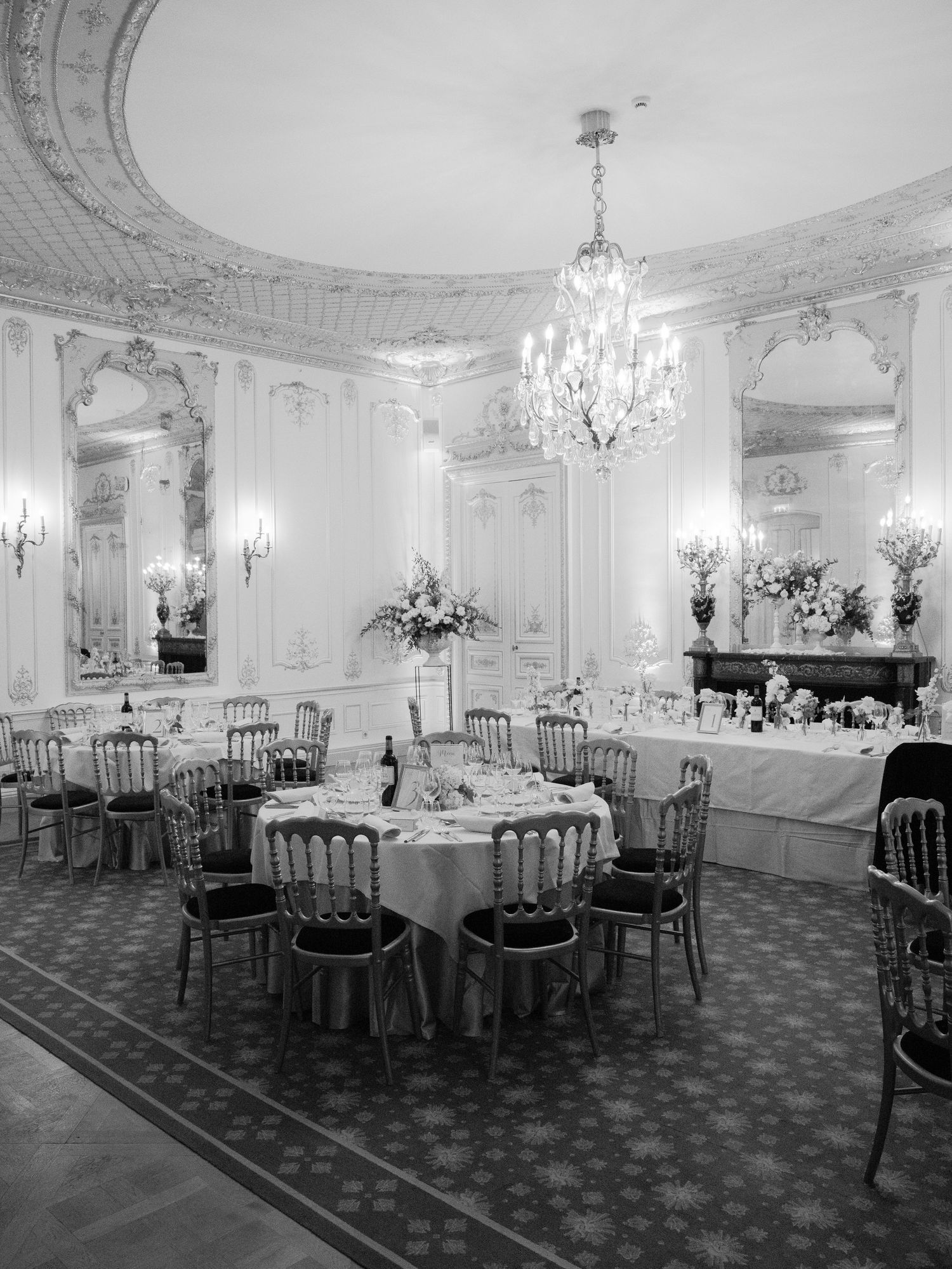 Classic black and white photo of an elegant ballroom with round tables and crystal chandeliers.
