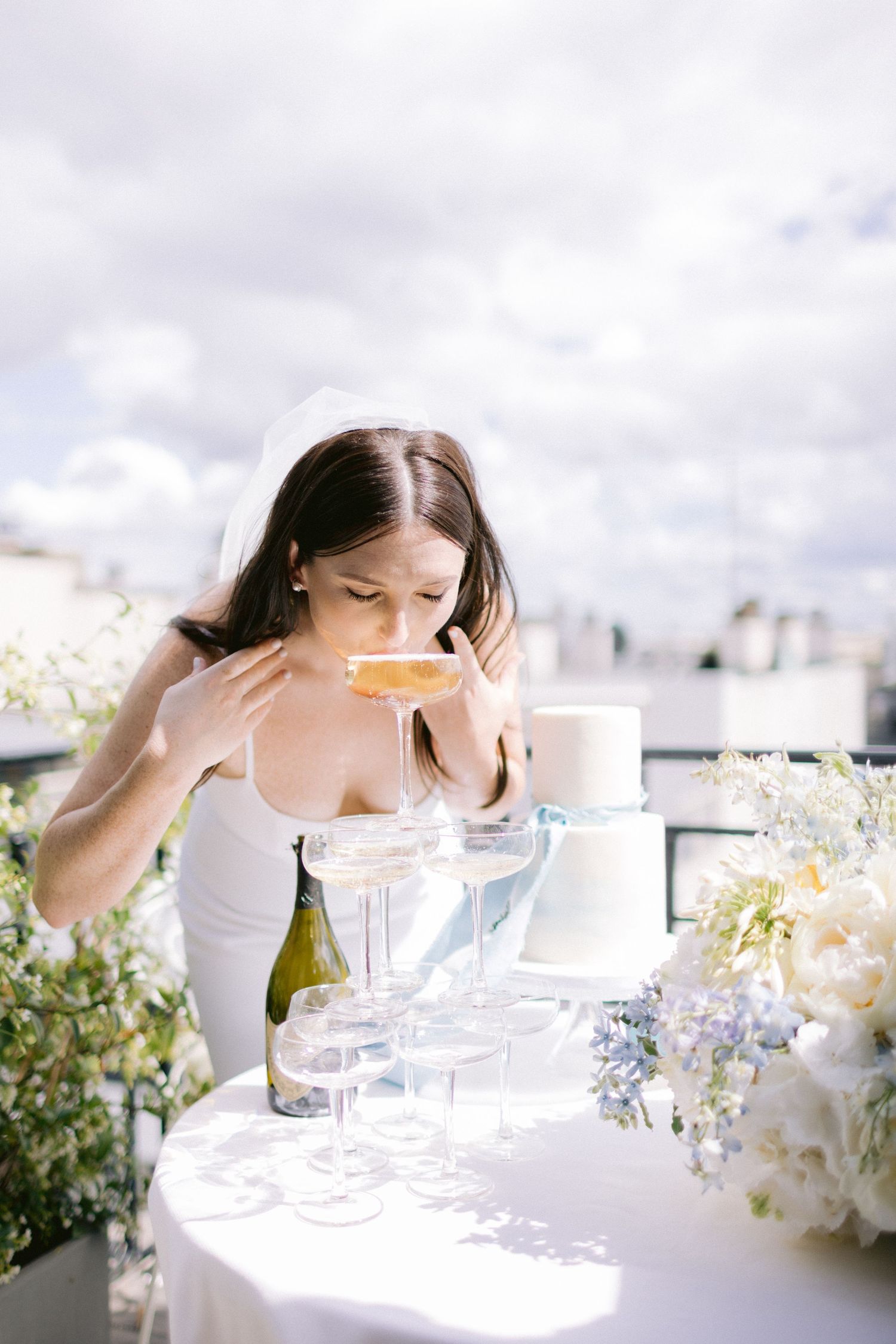 Close-up of champagne glasses being arranged on a rooftop with white floral arrangements.