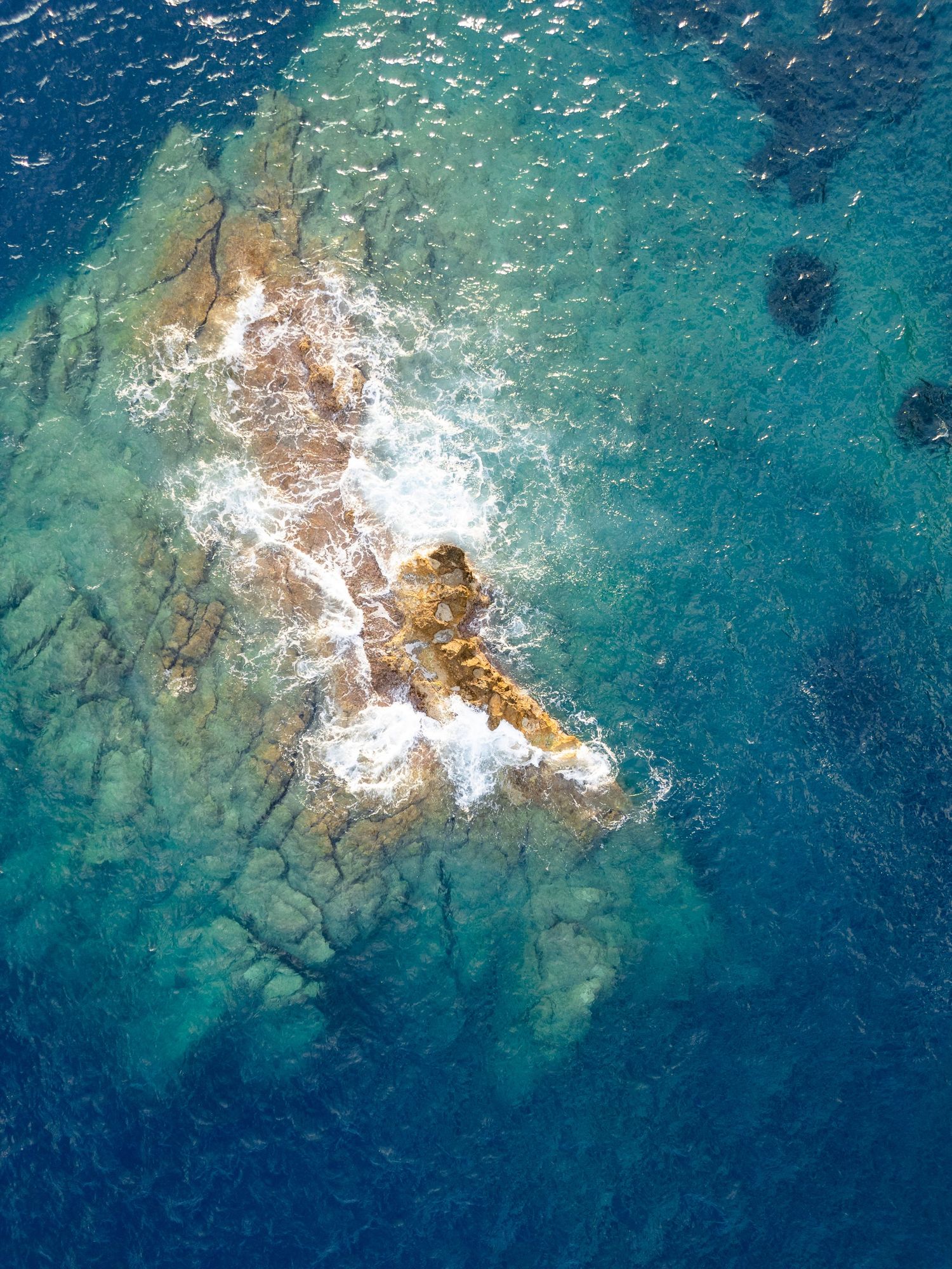 Aerial view of crystal clear turquoise waters crashing against rocky Mediterranean coastline.