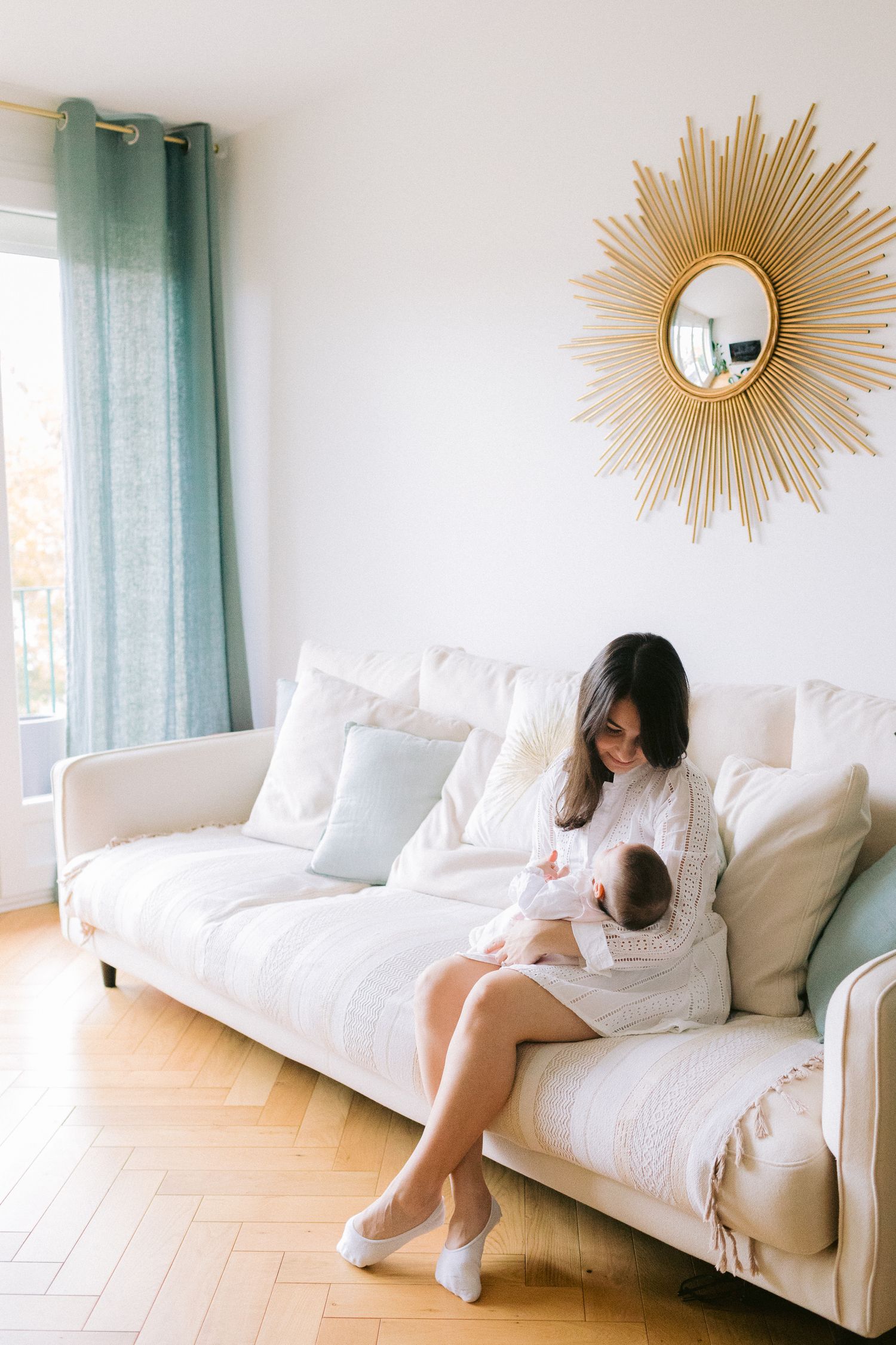 A cozy living room scene on a white sofa with a sunburst mirror on the wall.