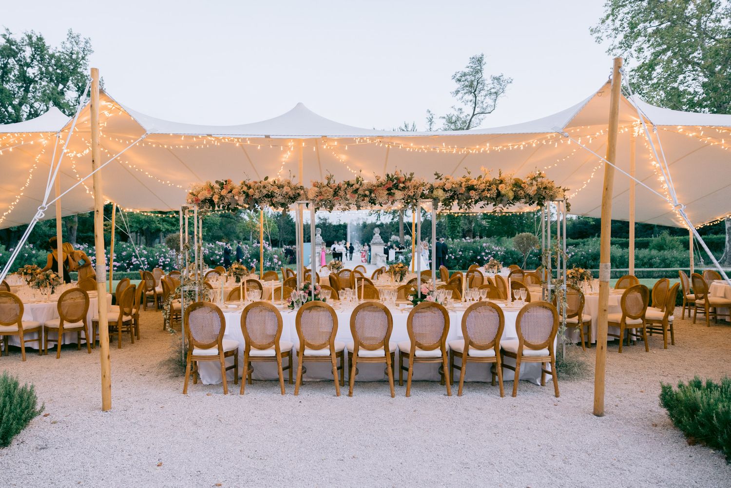Elegant outdoor wedding reception setup with long tables under stretch tent lighting.