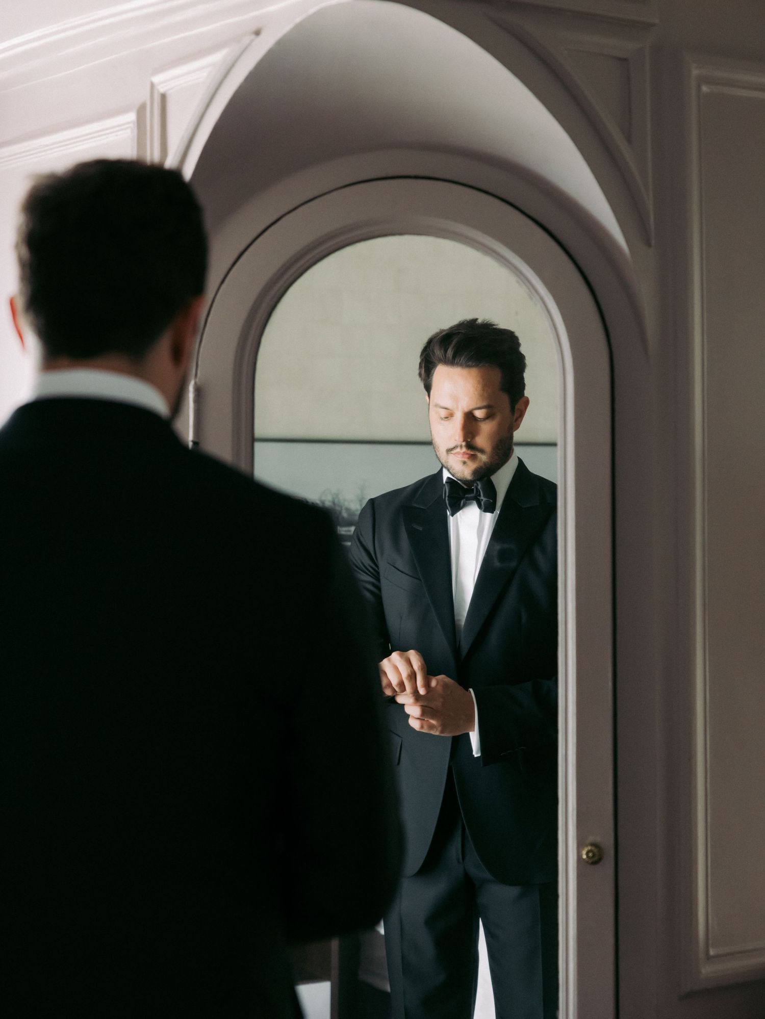 Silhouette of a person in formal attire standing in an arched doorway.