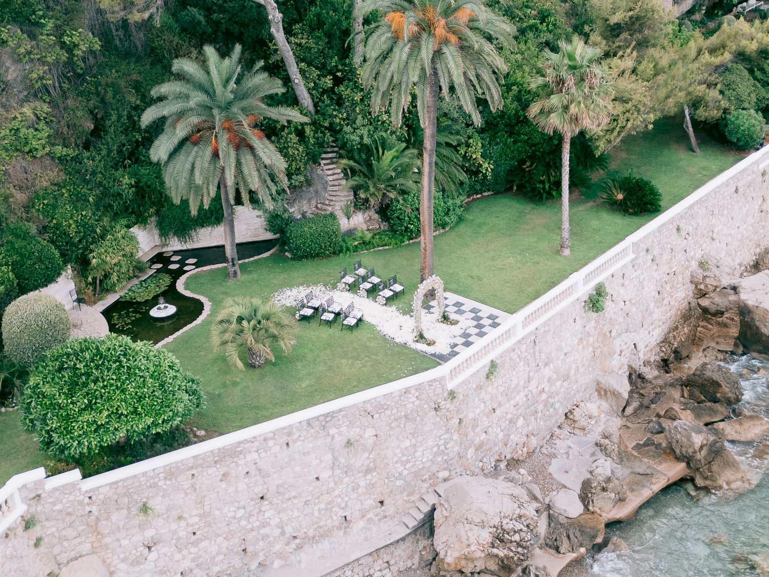 Aerial view of a coastal property with palm trees and stone pathways leading to the water.