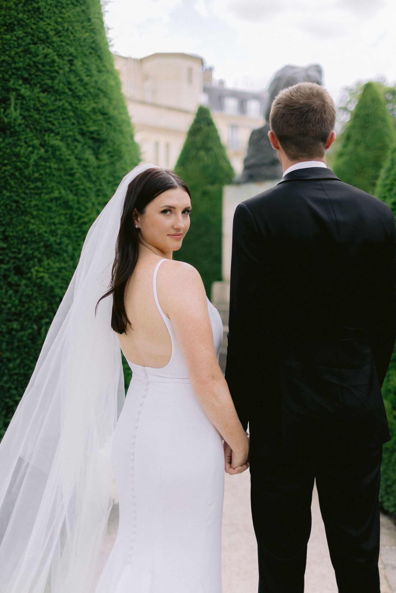 A couple walks through a formal garden with tall hedges creating a romantic pathway.