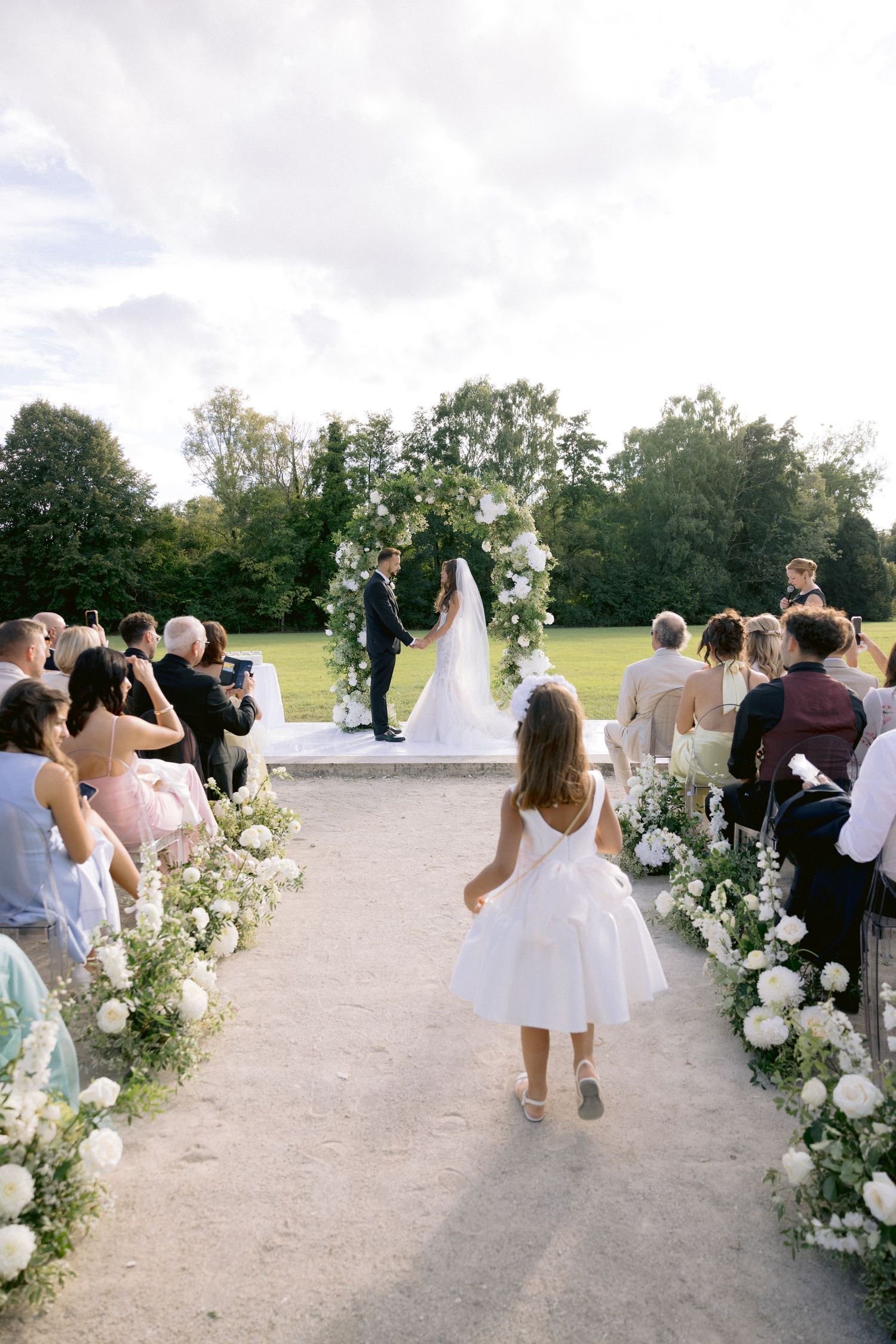 Wedding guests walking along a path lined with white floral arrangements.
