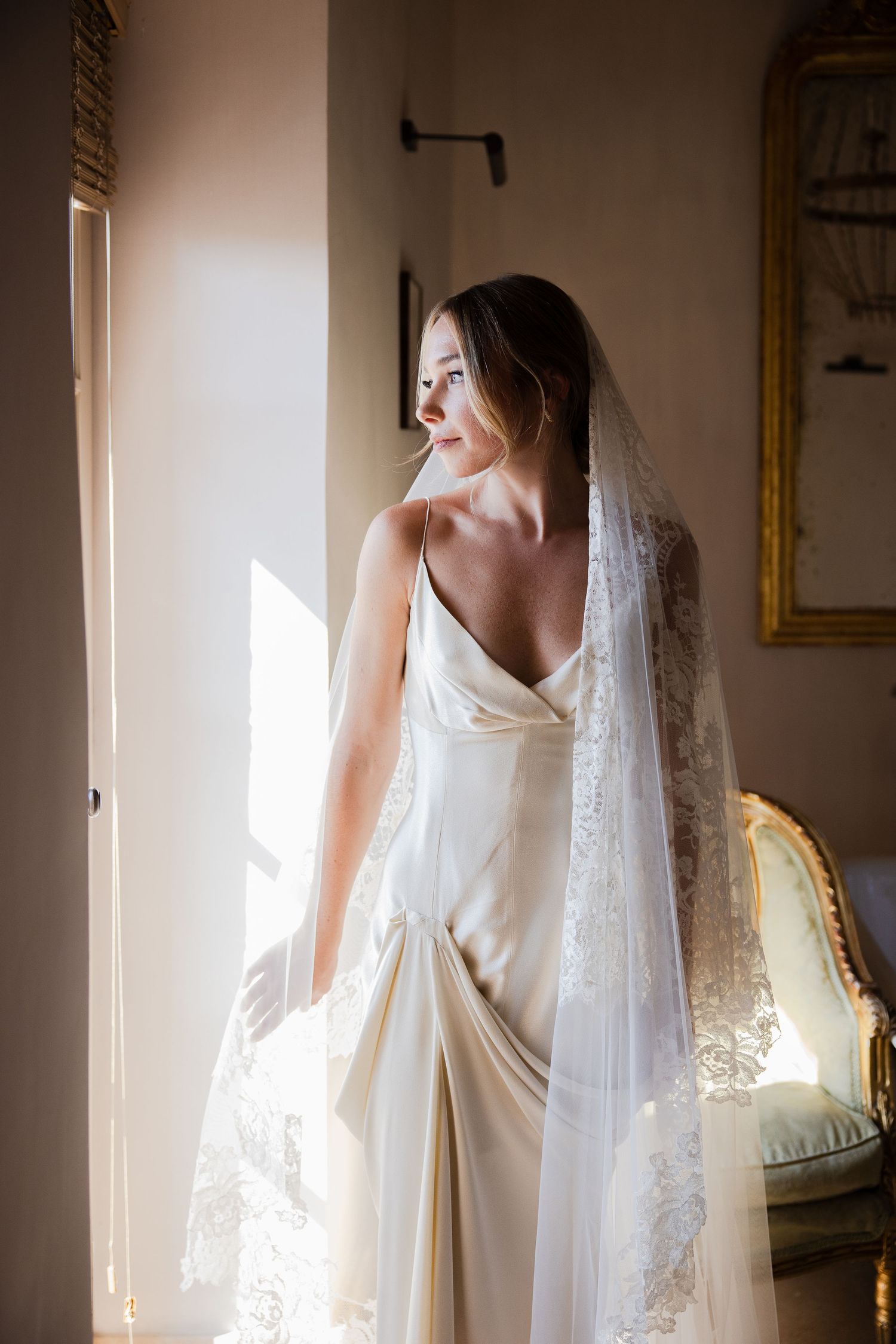 Classic white wedding dress with veil photographed near a sunlit window.