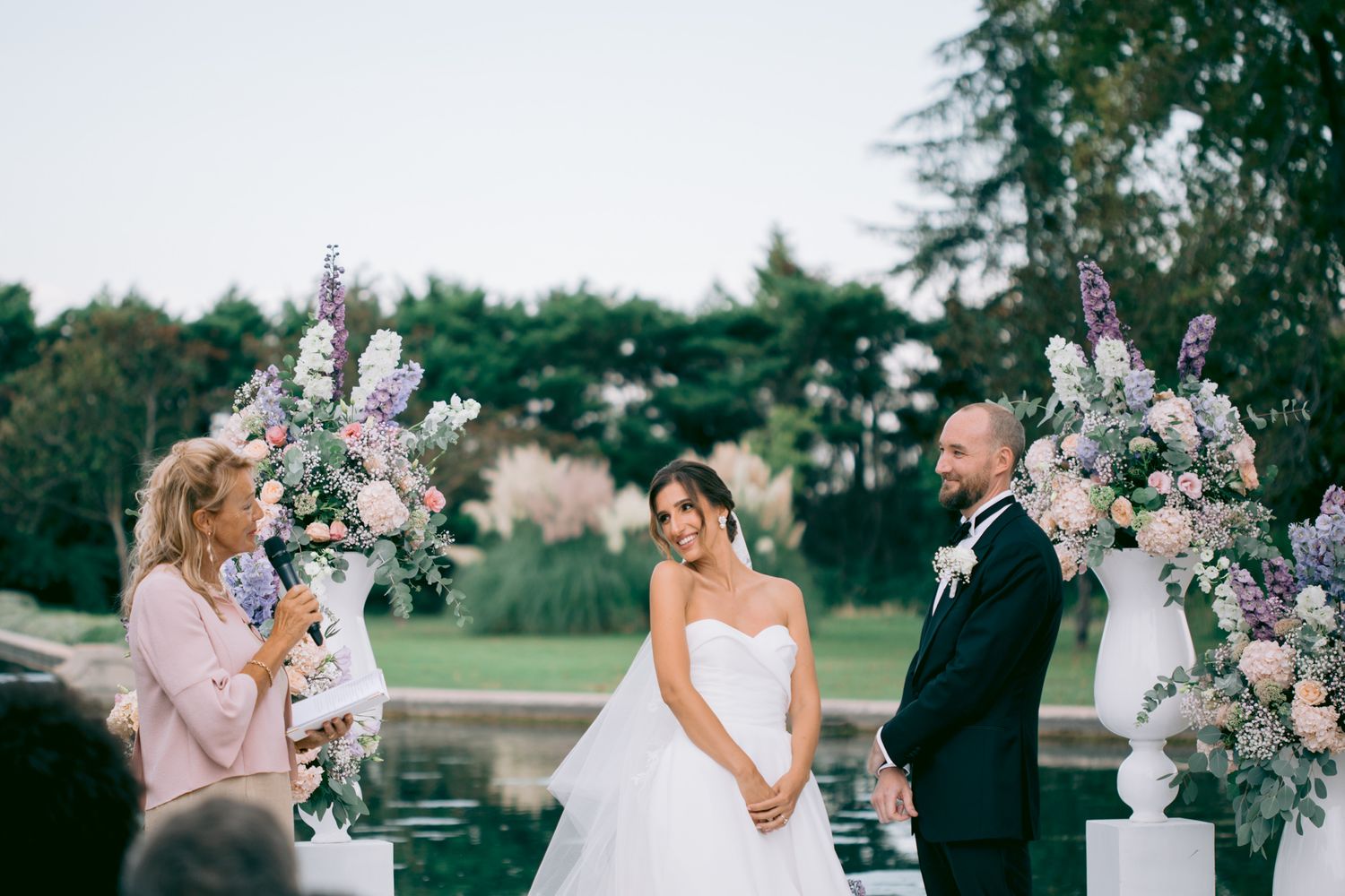 An outdoor wedding ceremony features elegant floral arrangements in pink and purple hues.