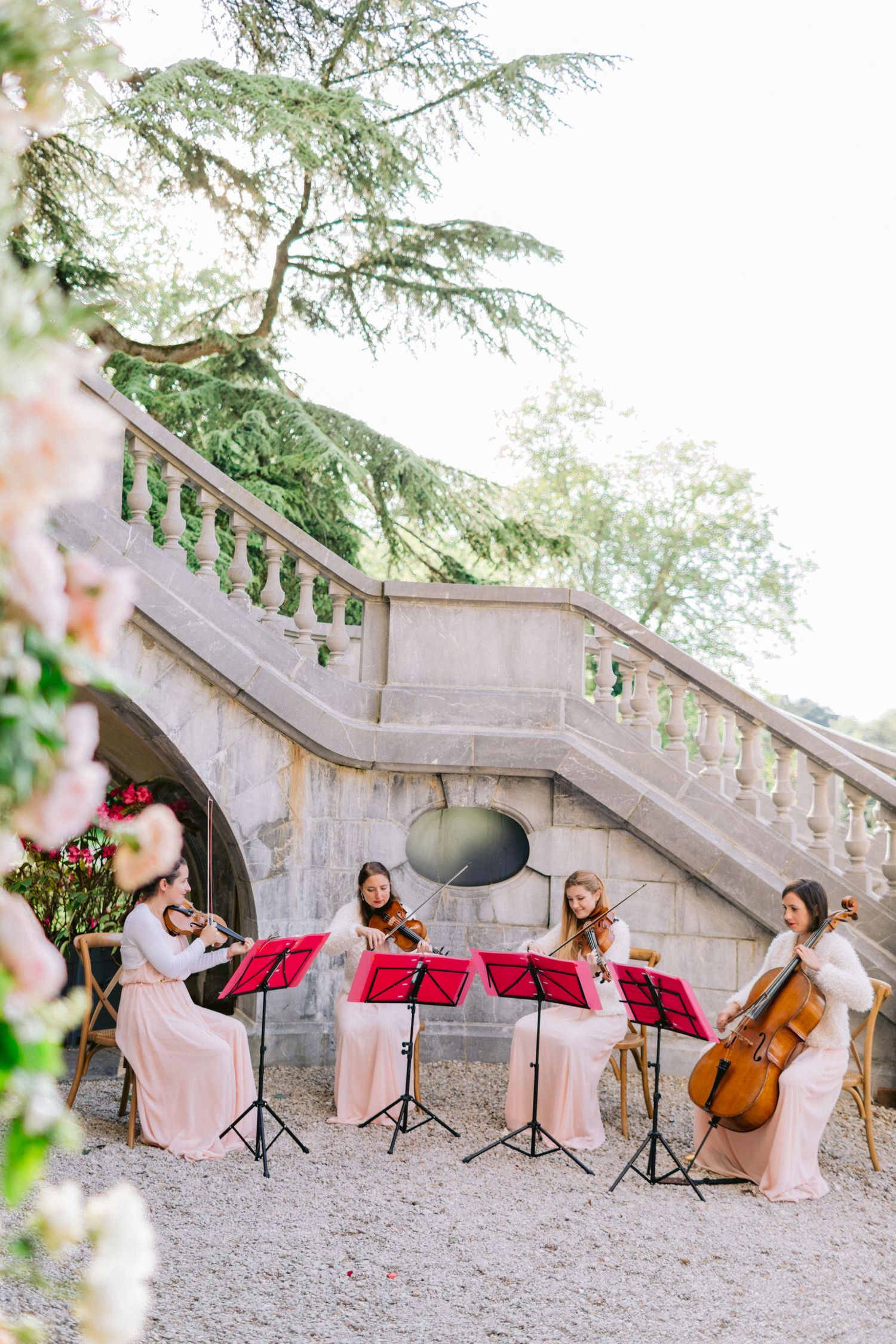 String quartet musicians performing at an outdoor wedding by stone steps.