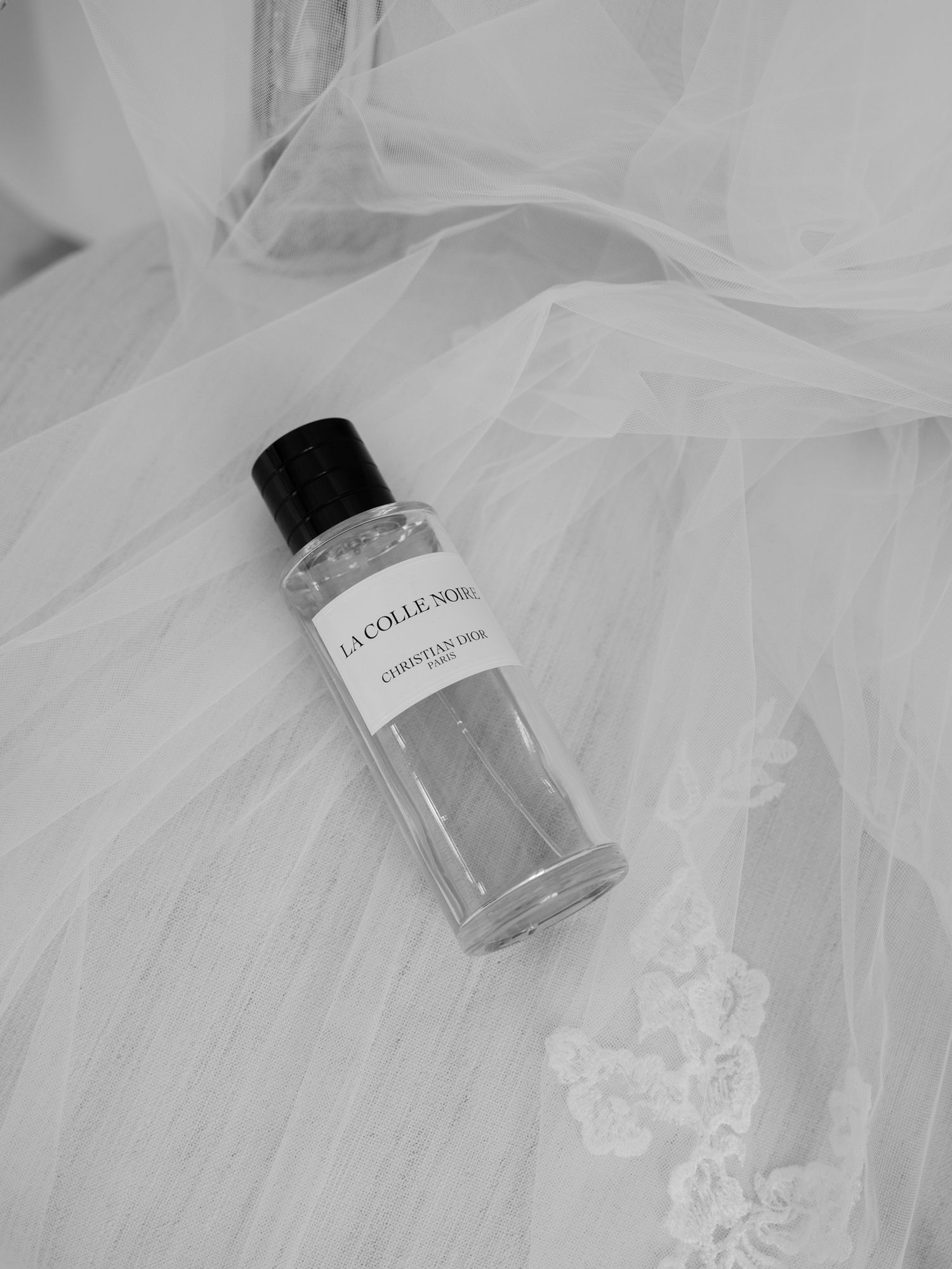 Perfume bottle placed delicately on white tulle fabric in black and white.
