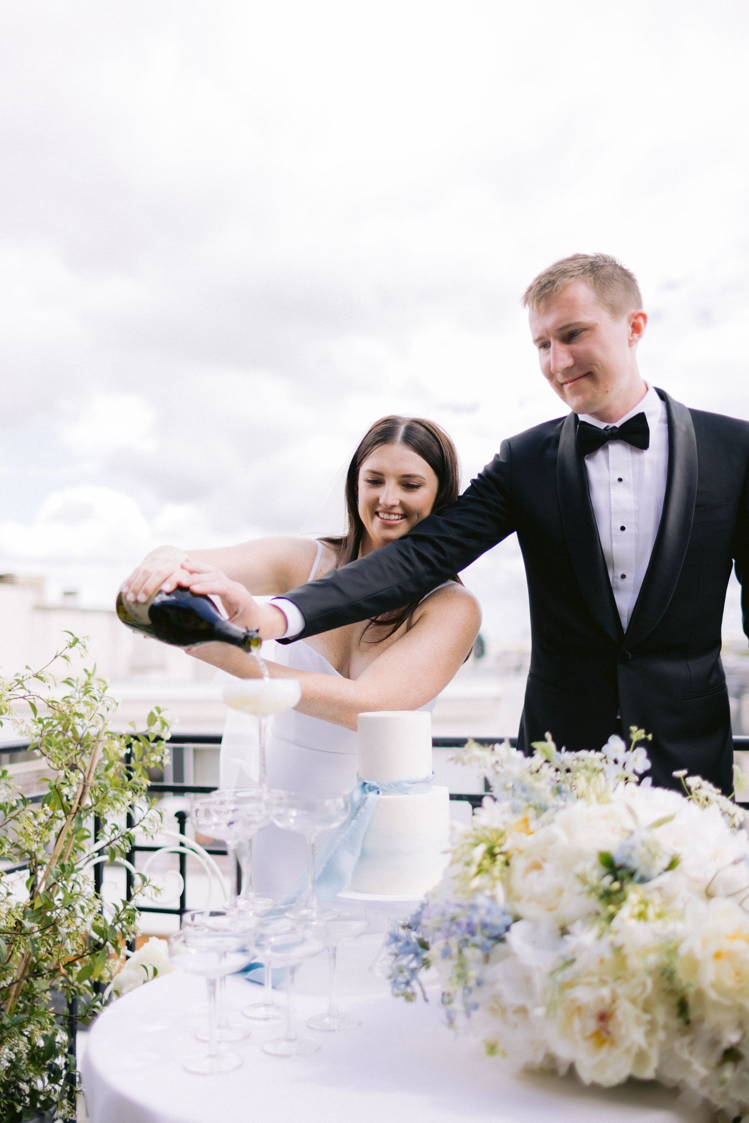 Newlyweds sharing champagne on an elegant rooftop terrace with white floral decorations.