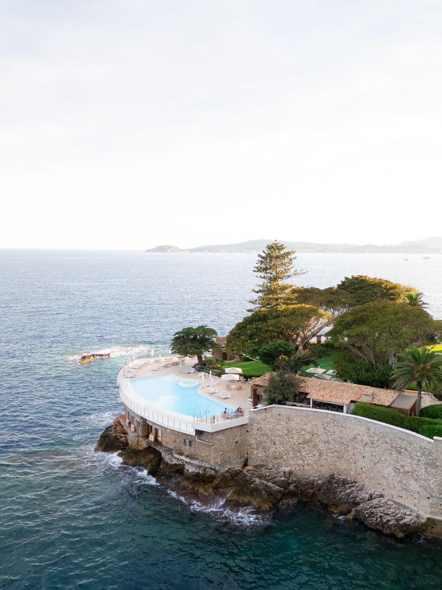 Panoramic view of a seaside venue with infinity pool built into rocky cliffs above blue waters.