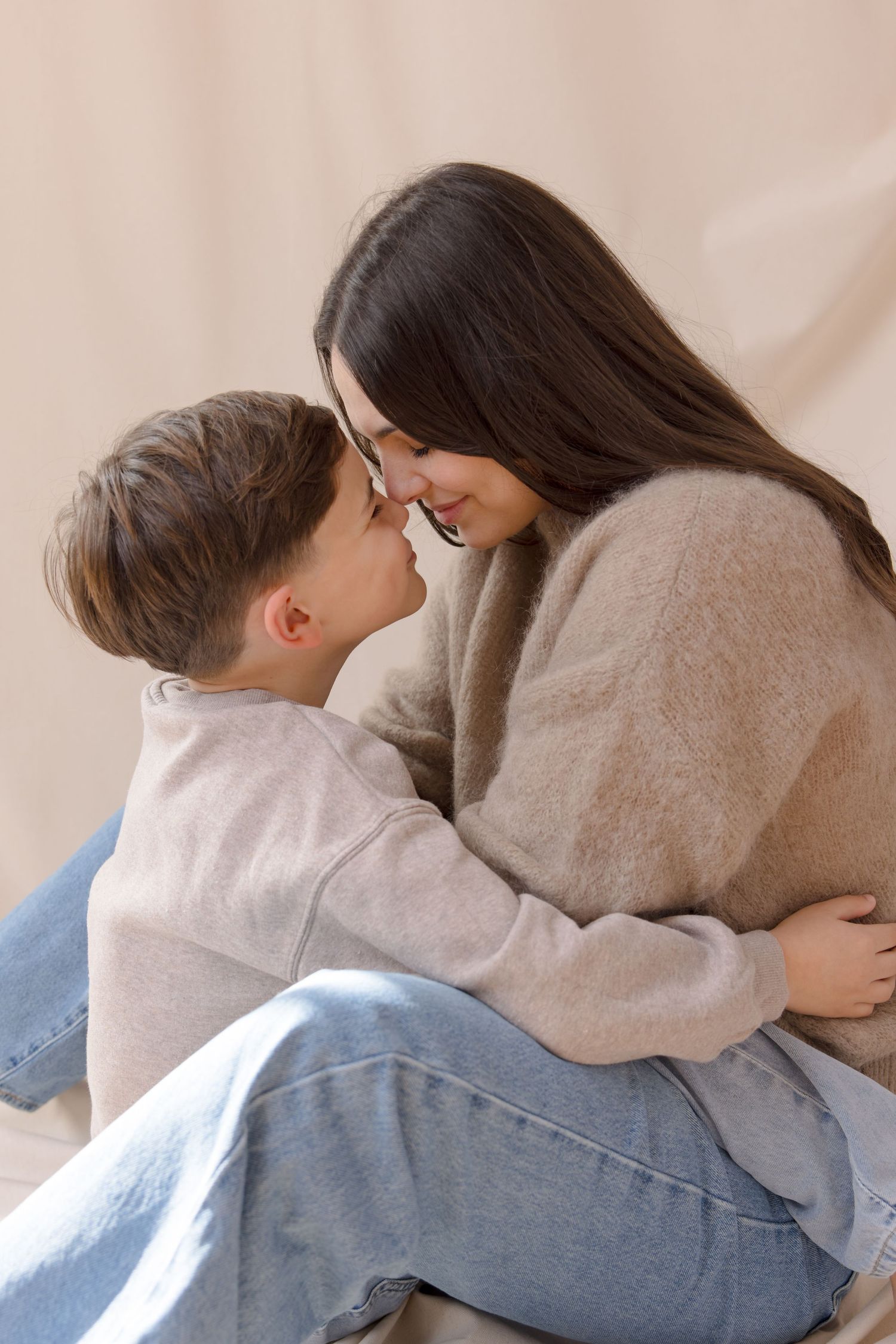 A young couple in beige sweaters sharing a tender nose-to-nose moment while embracing warmly.