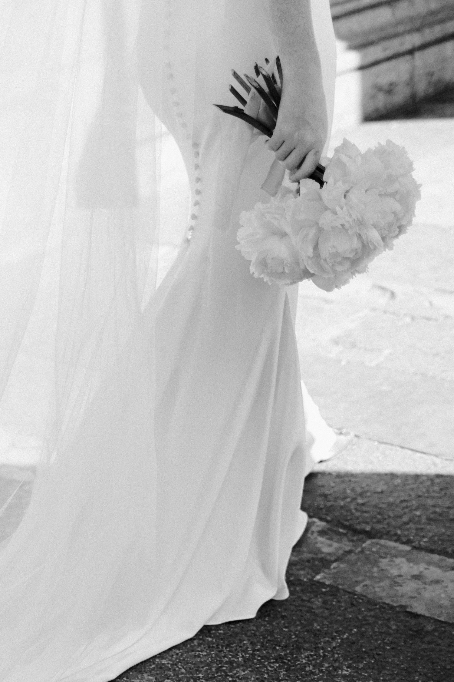 Black and white detail of wedding dress hem and white peony bouquet.