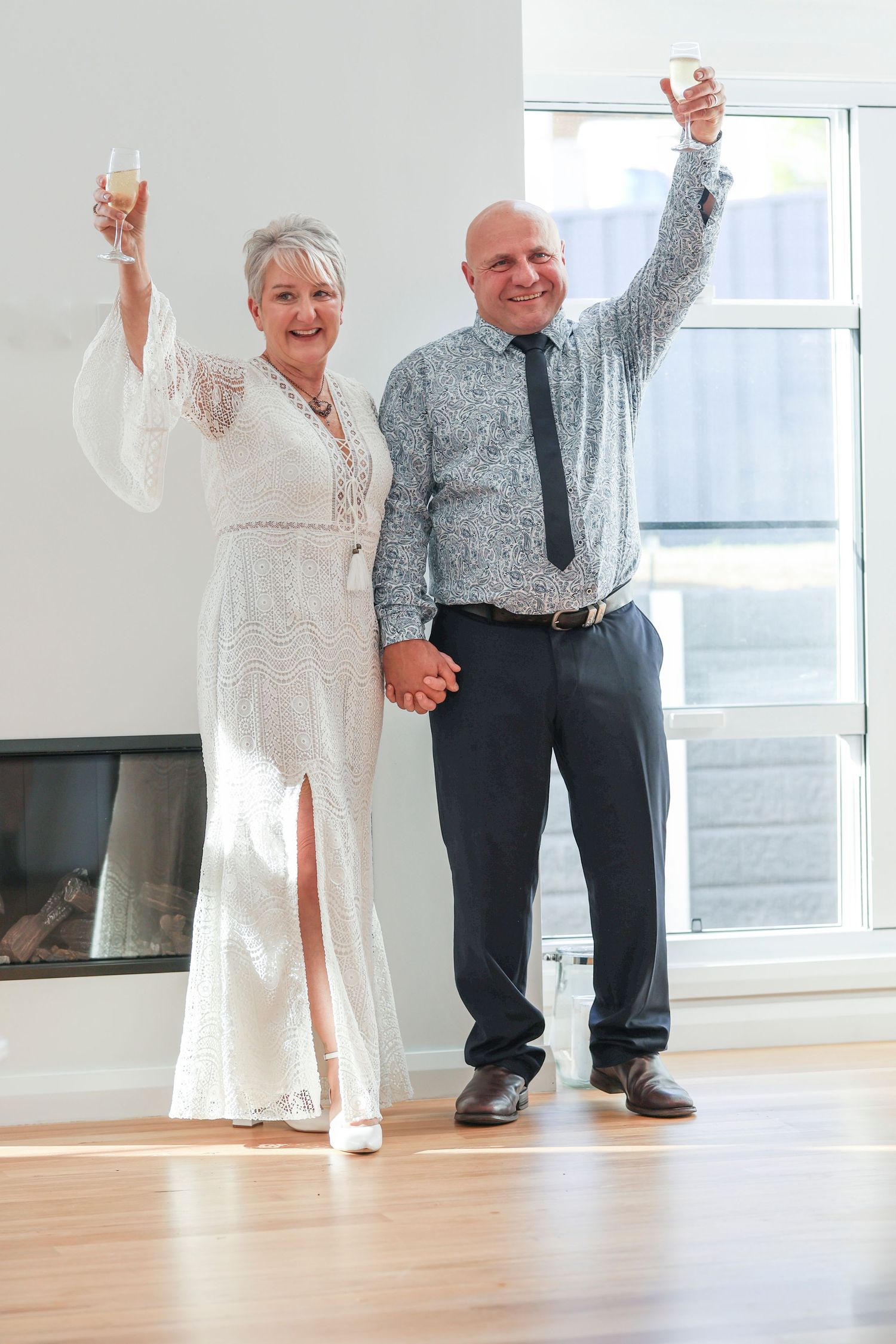 A couple in formal attire raises their glasses in celebration on a bright indoor setting.