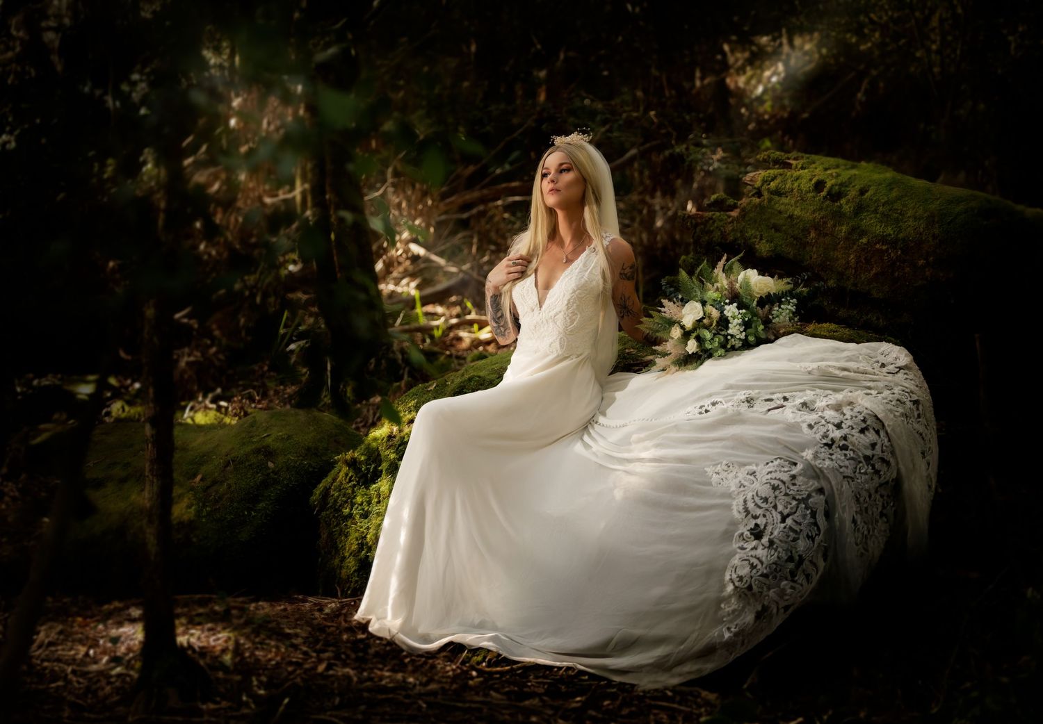 A flowing white wedding dress billows dramatically in a moody forest setting with natural foliage and filtered sunlight.