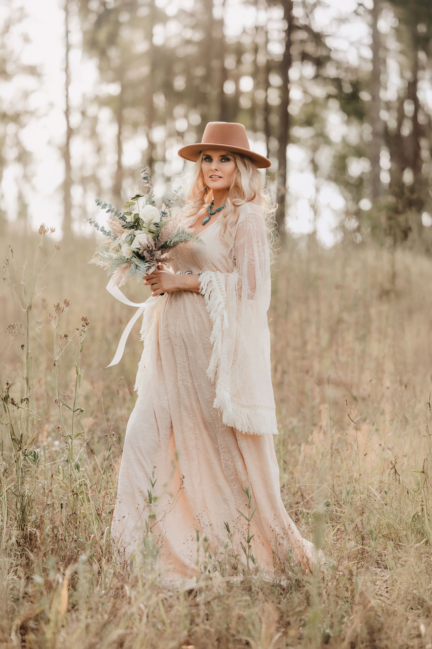 Boho styled portrait in neutral dress holding wildflower bouquet in autumn field.