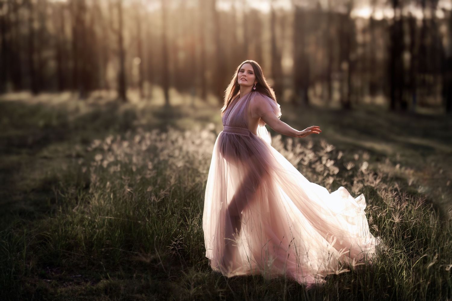 A flowing pink dress twirls gracefully in a sunlit forest meadow during golden hour.