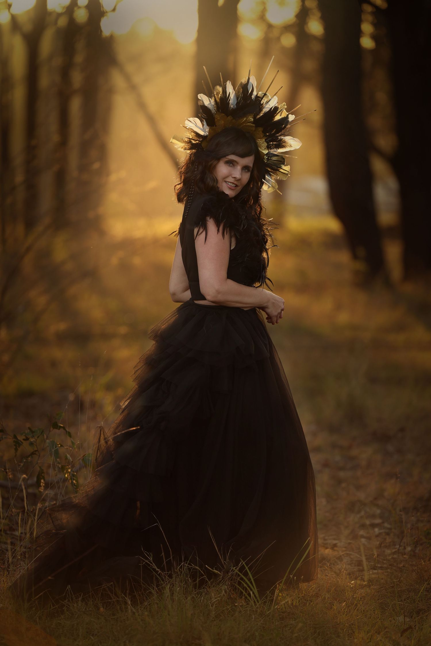 Dramatic black tulle gown and feathered crown photographed in moody autumn forest setting.