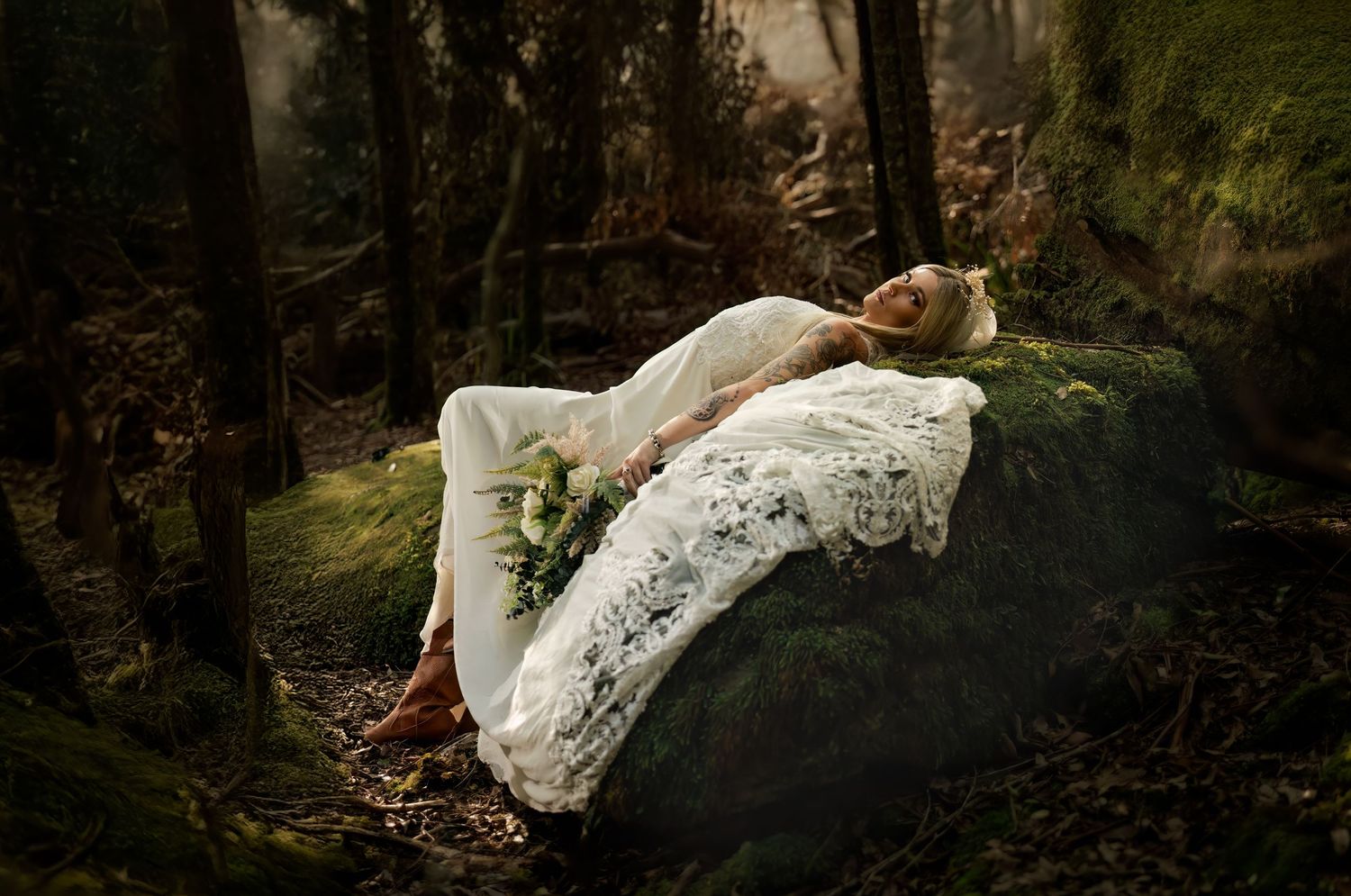 A figure in a white lace dress lies peacefully on a moss-covered rock in an ethereal forest setting.