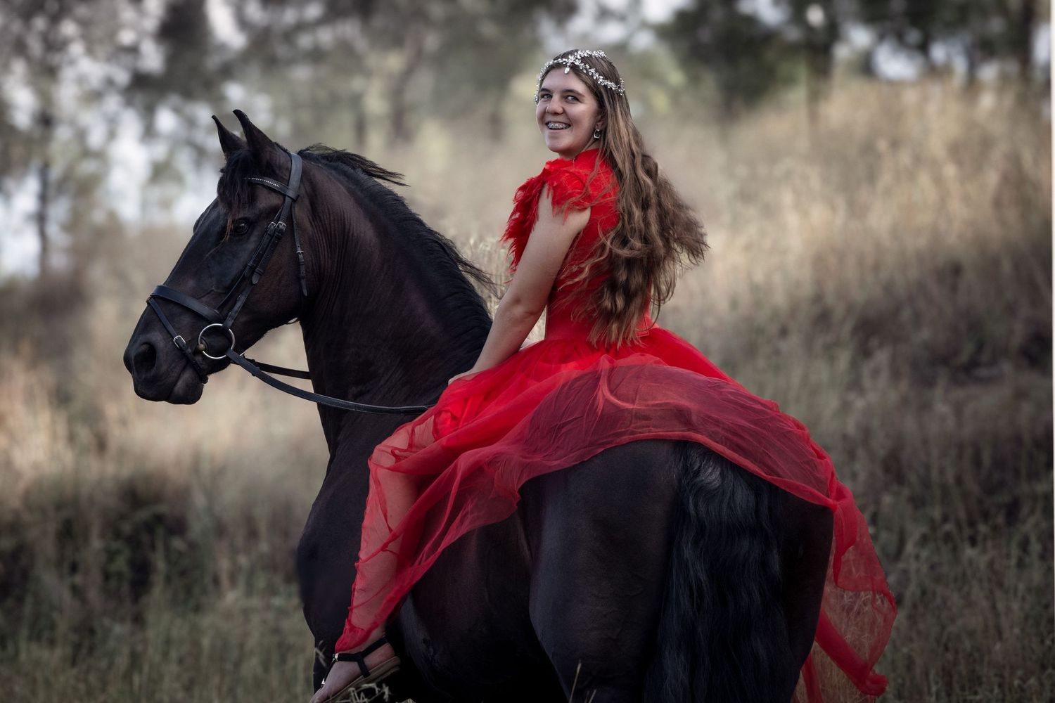 Dramatic equestrian portrait with flowing red dress on black horse in misty field.