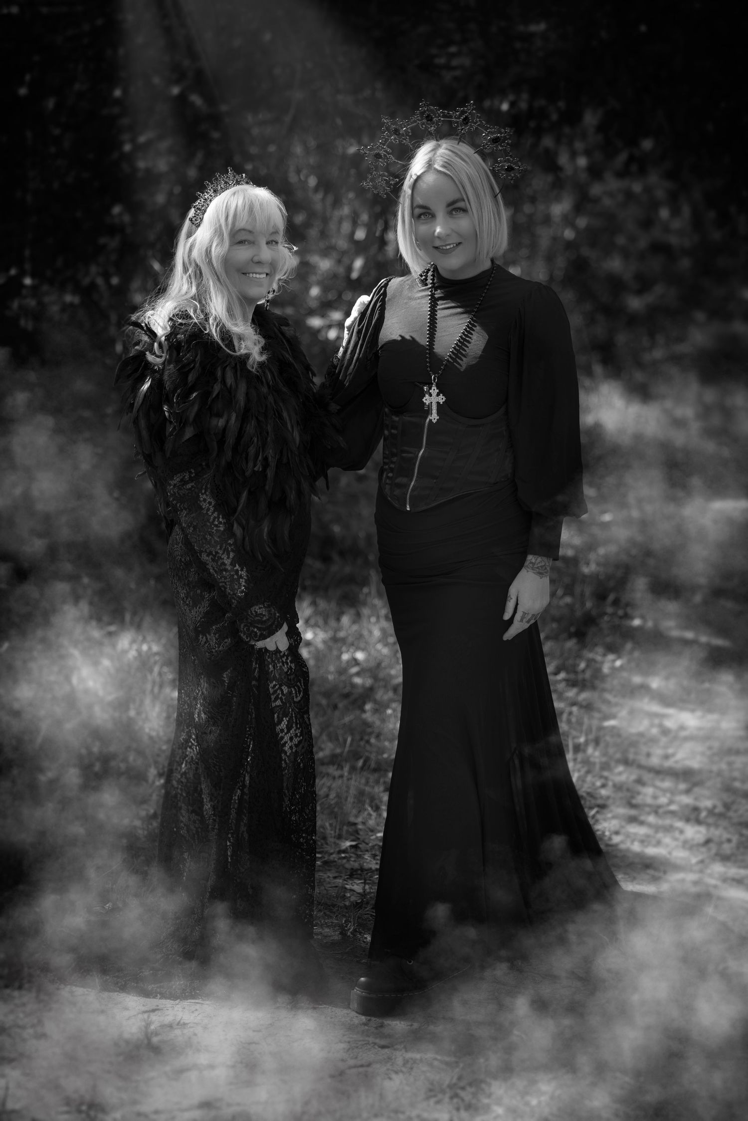 Atmospheric black and white portrait of two people in dark dresses surrounded by fog.