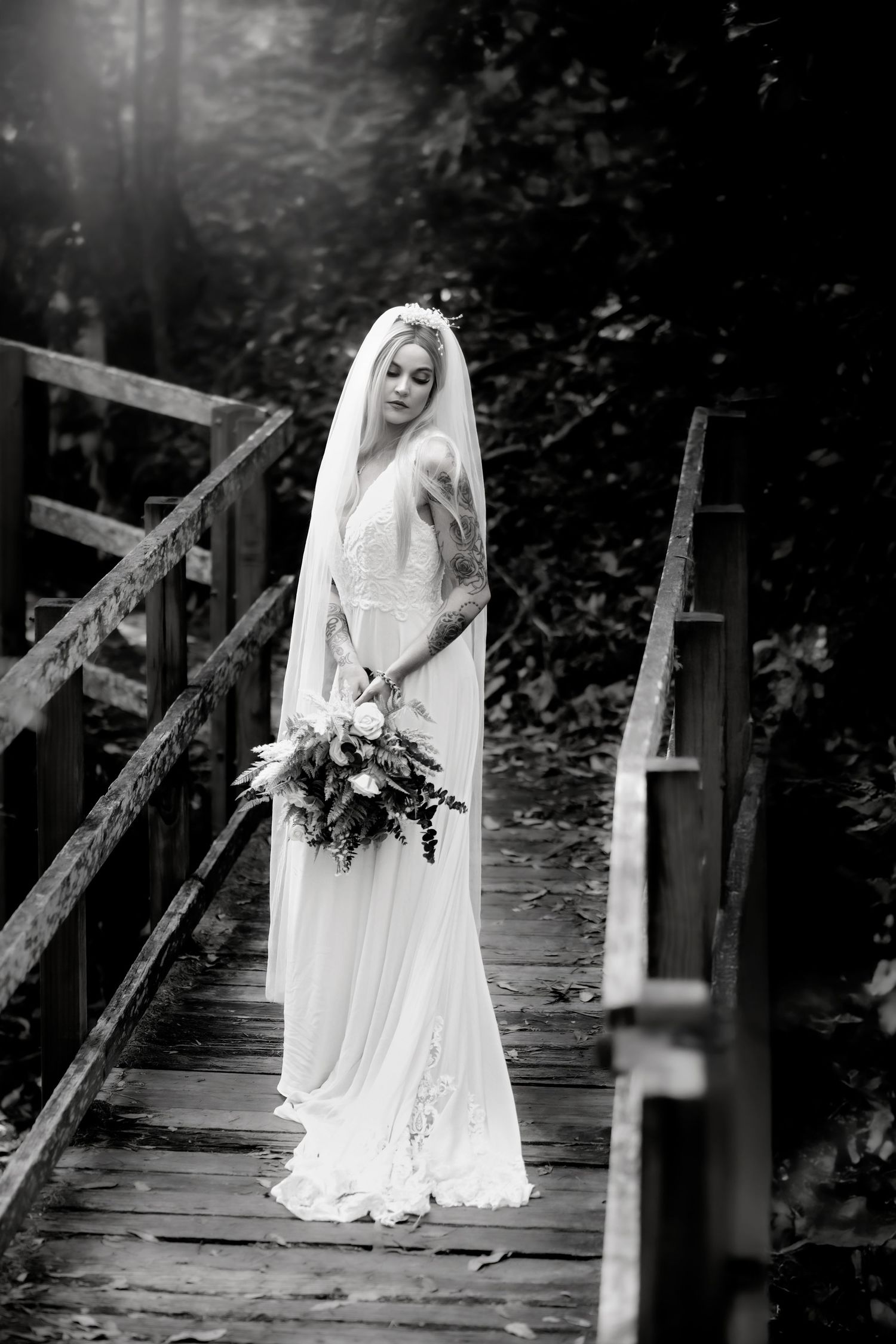 Classic black and white bridal portrait on wooden bridge with long veil and bouquet.