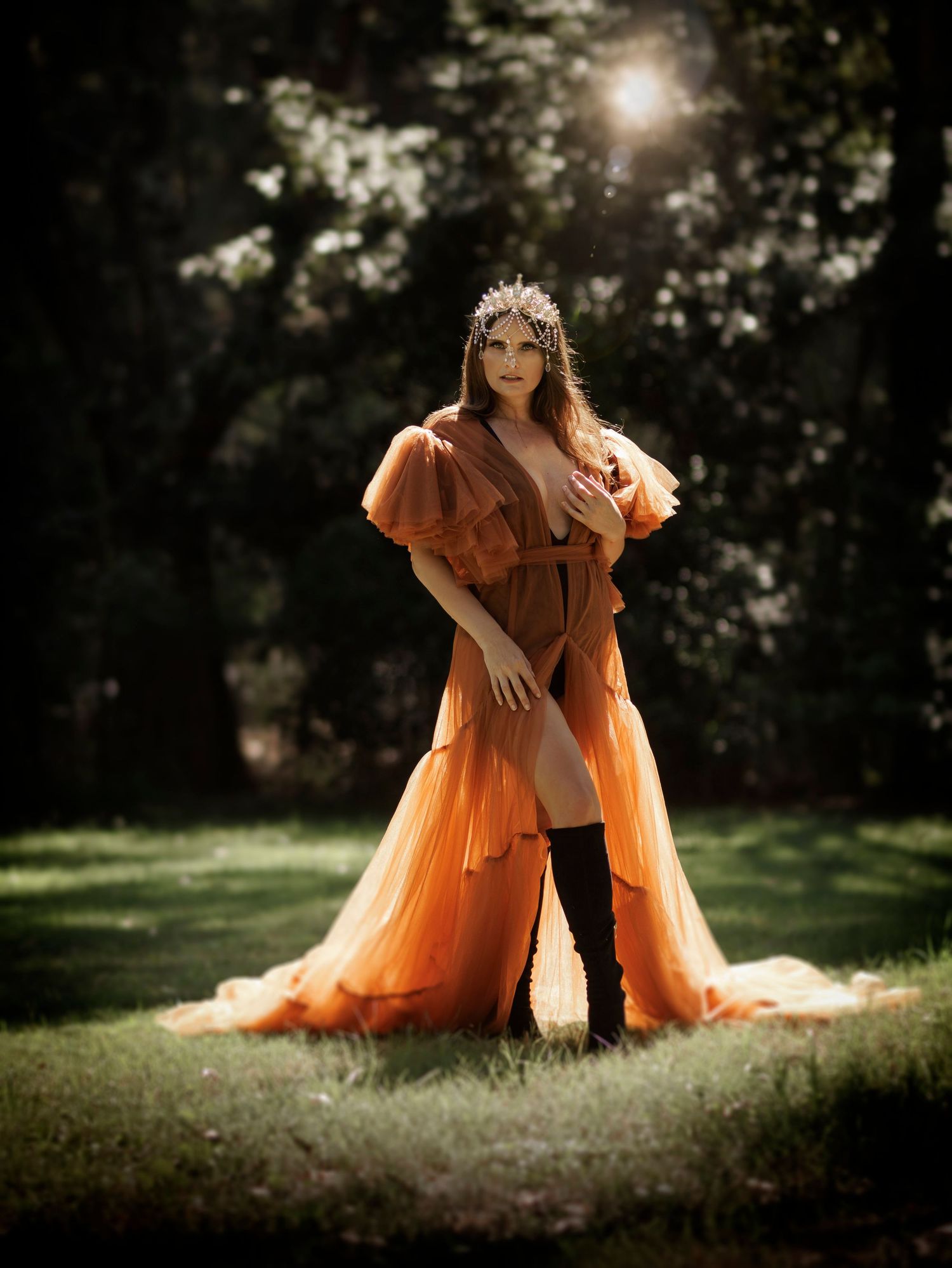 Ethereal orange tulle dress captured in magical backlit forest setting with sunburst effect.