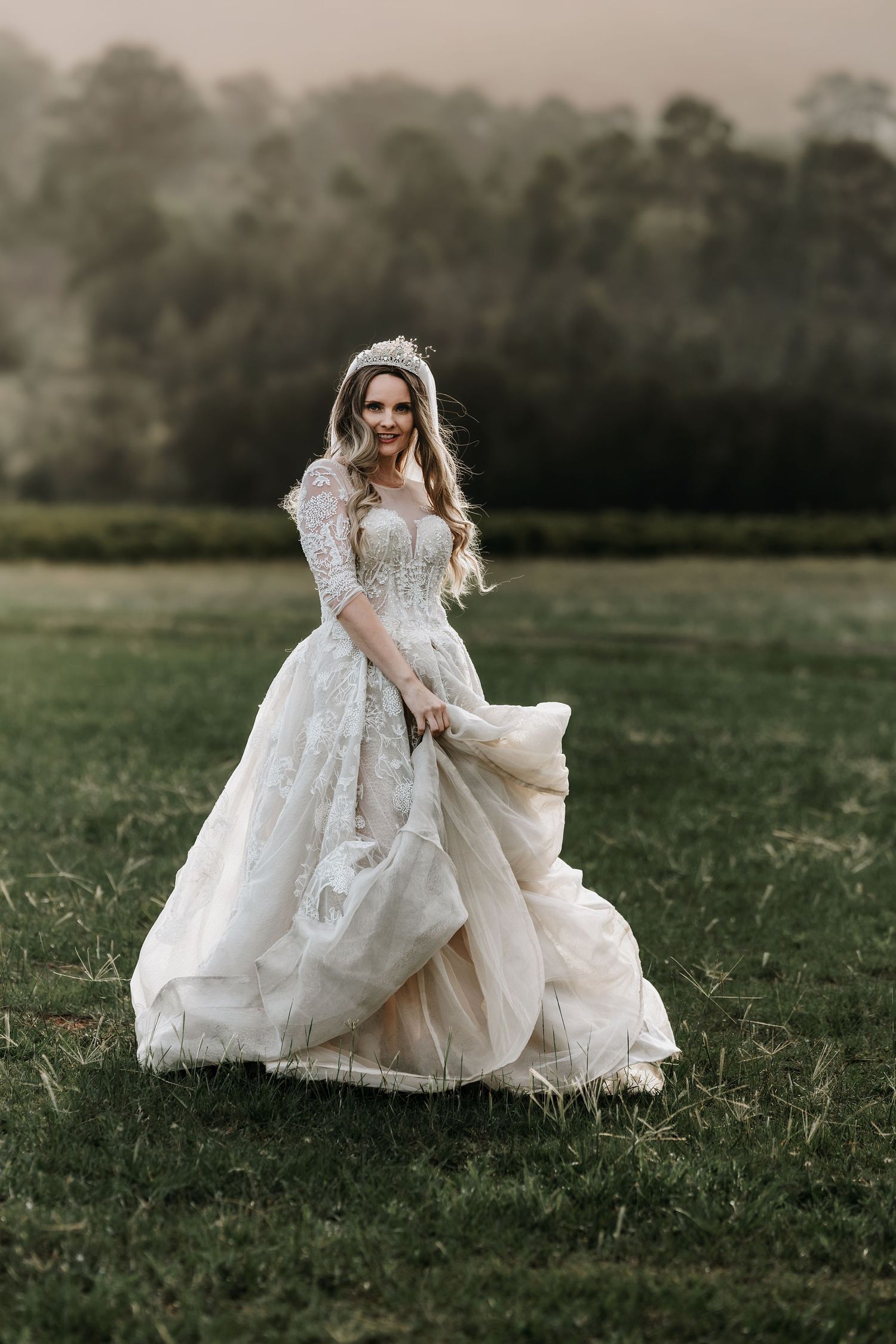 Elegant bride in a flowing lace wedding dress twirling in a misty meadow at dusk.