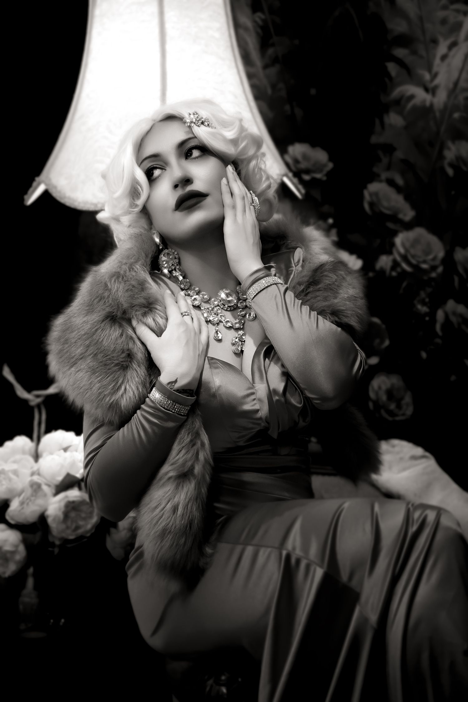 Dramatic black and white glamour portrait with platinum hair, fur collar, and statement necklace in film noir style.