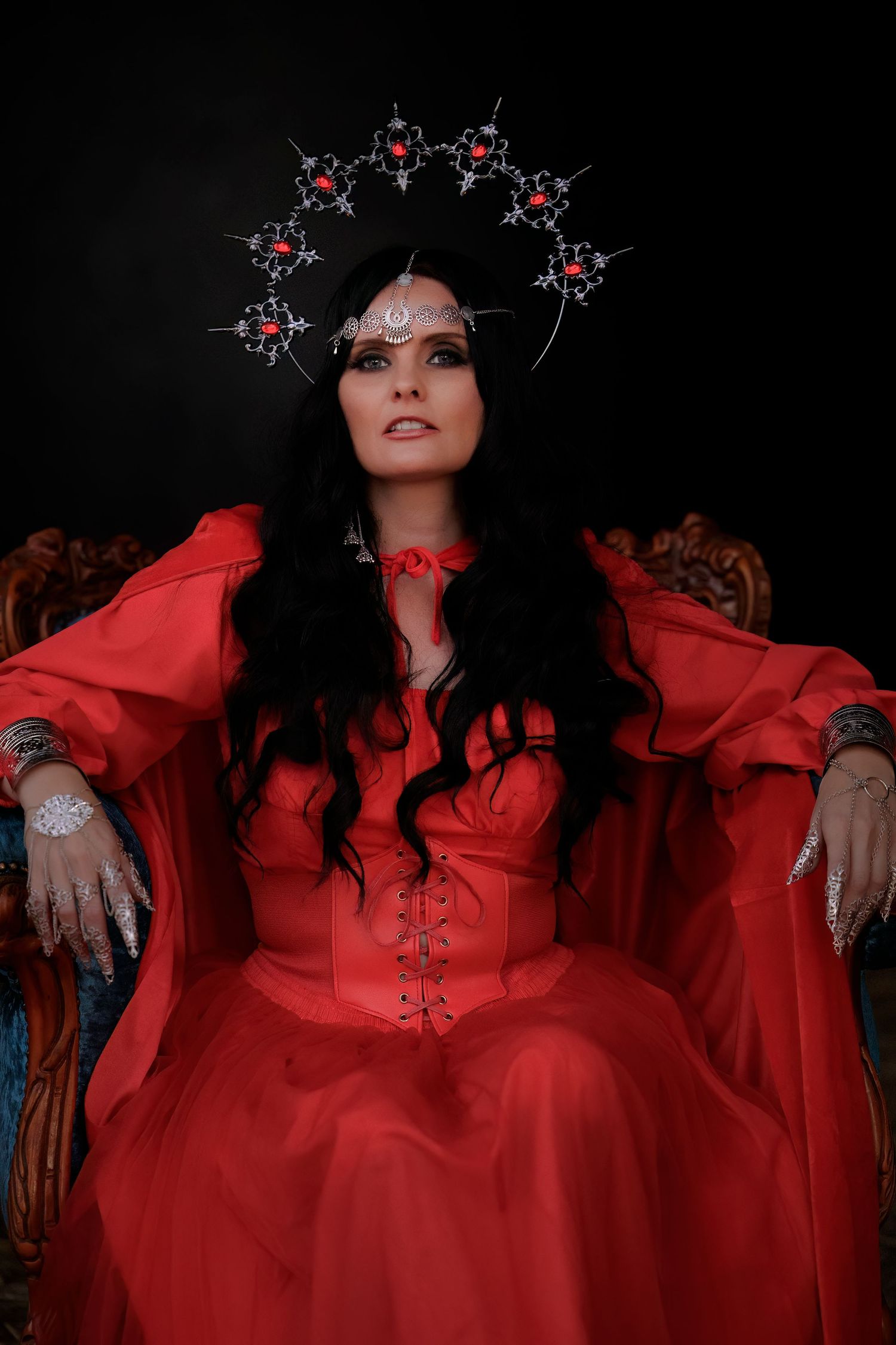 Gothic portrait in red dress with ornate crystal crown headpiece against dark background.