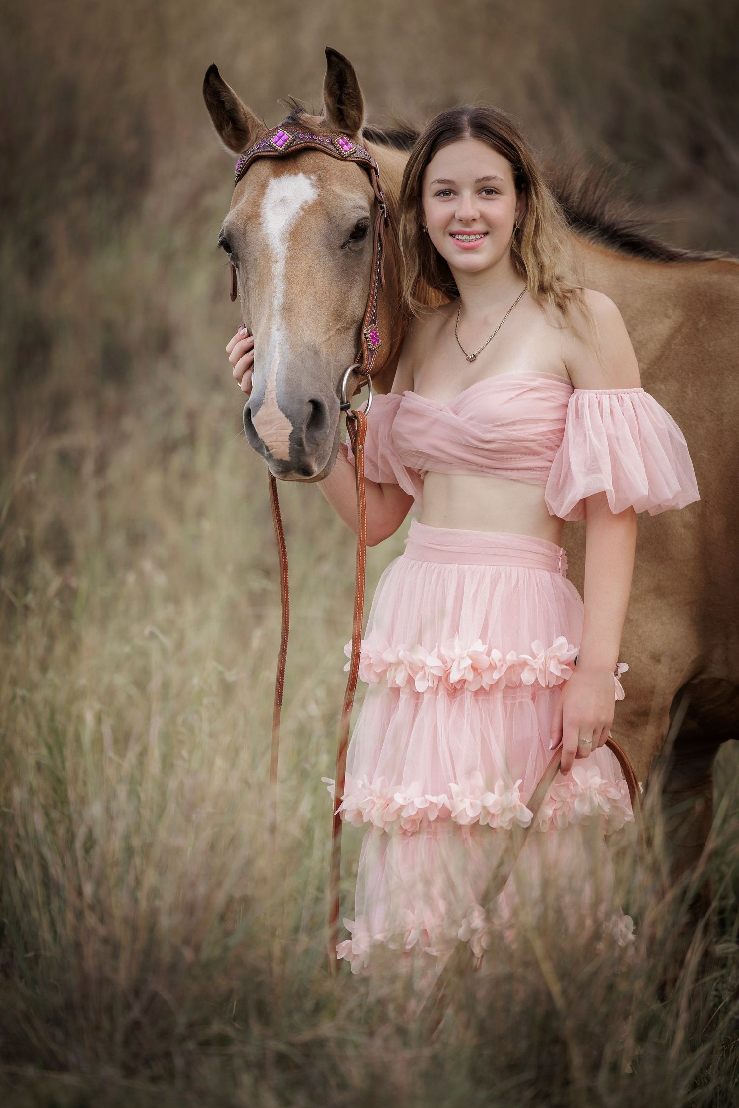 A pink two-piece dress complements the warm tones of a chestnut horse in this outdoor portrait.
