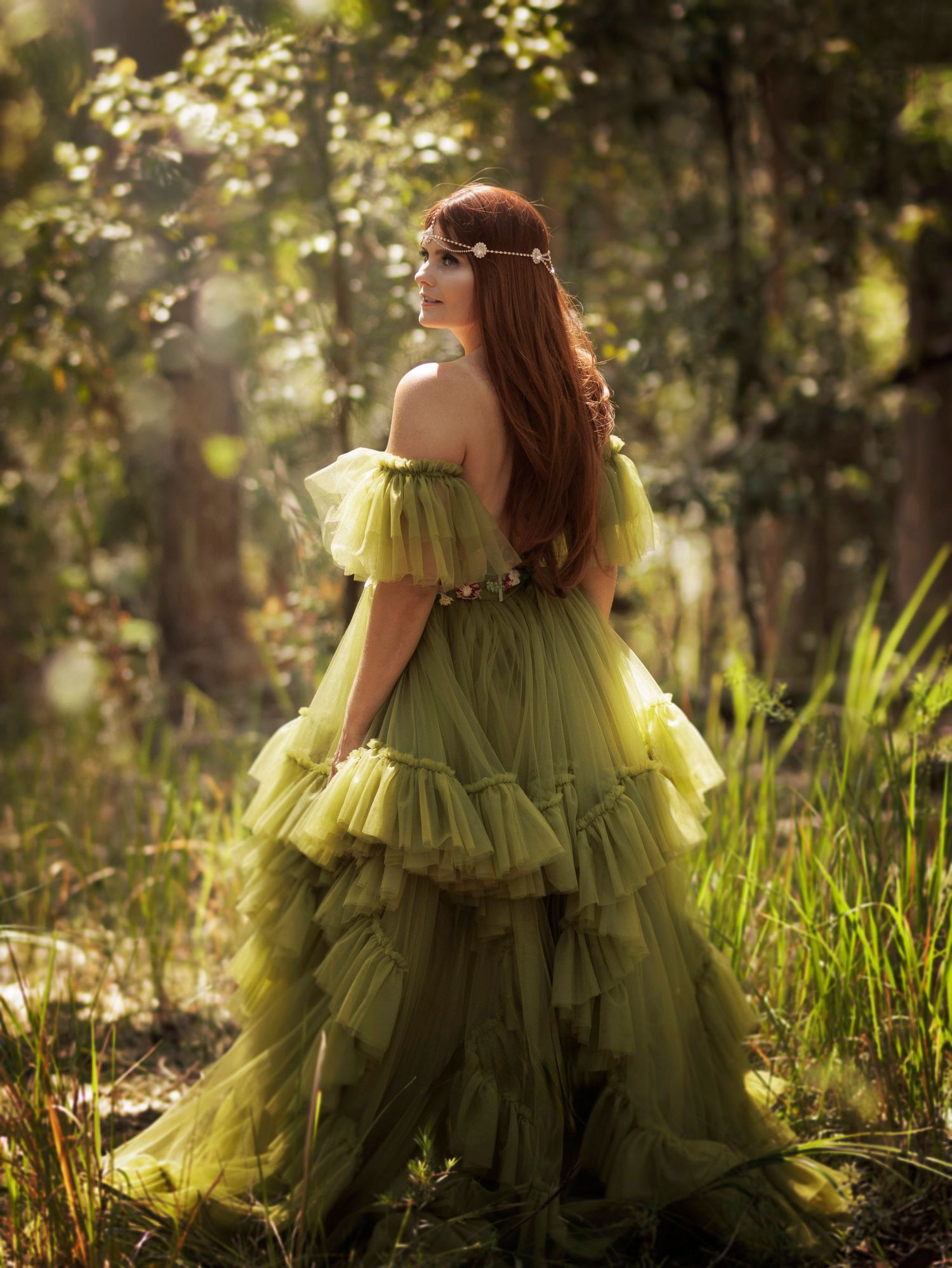 Person in flowing lime green tulle gown photographed from behind in enchanted forest setting.