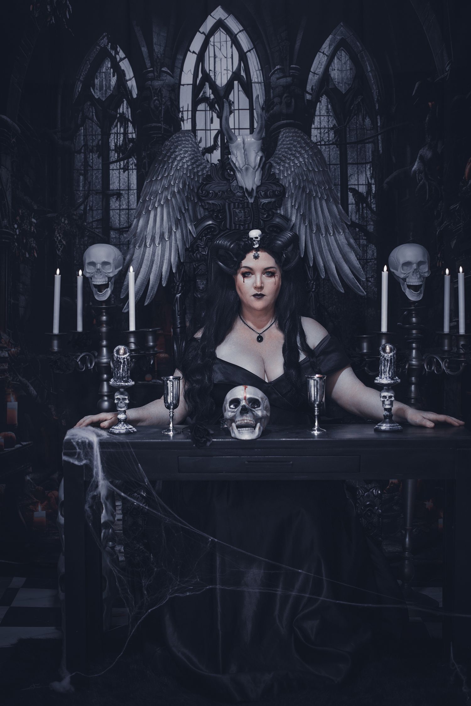 Dark gothic scene with candelabras, skulls and angel wings in a moody cathedral-like setting with black and blue tones.