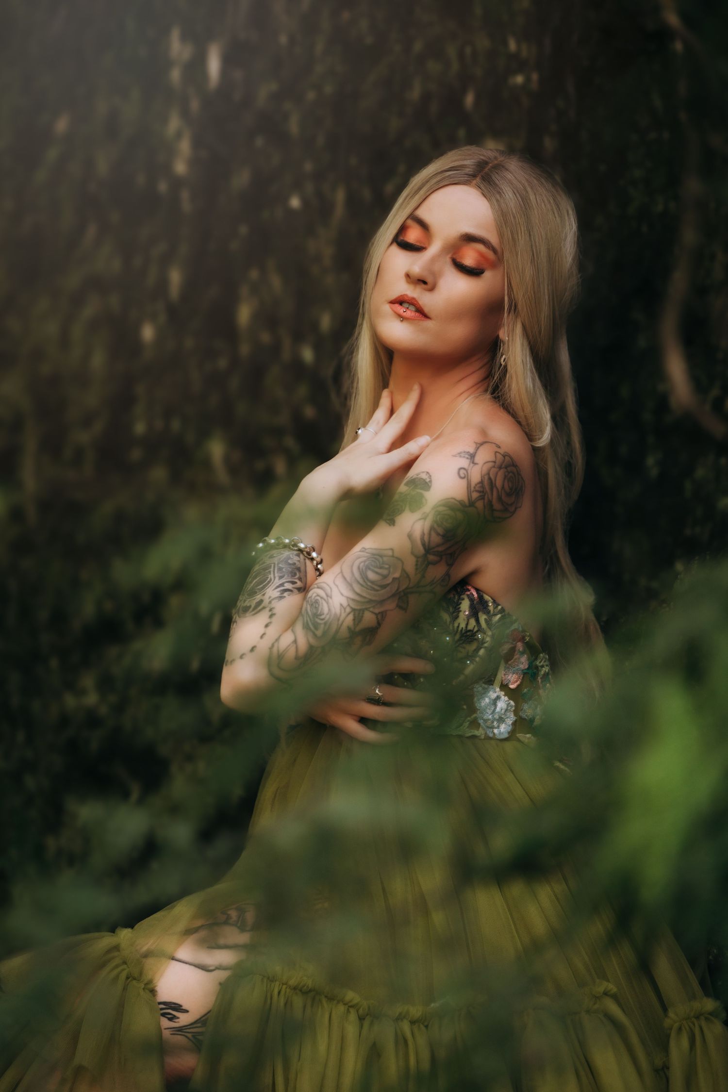 Ethereal portrait of a woman with tattoos posing in a misty green forest setting with soft dreamy lighting.