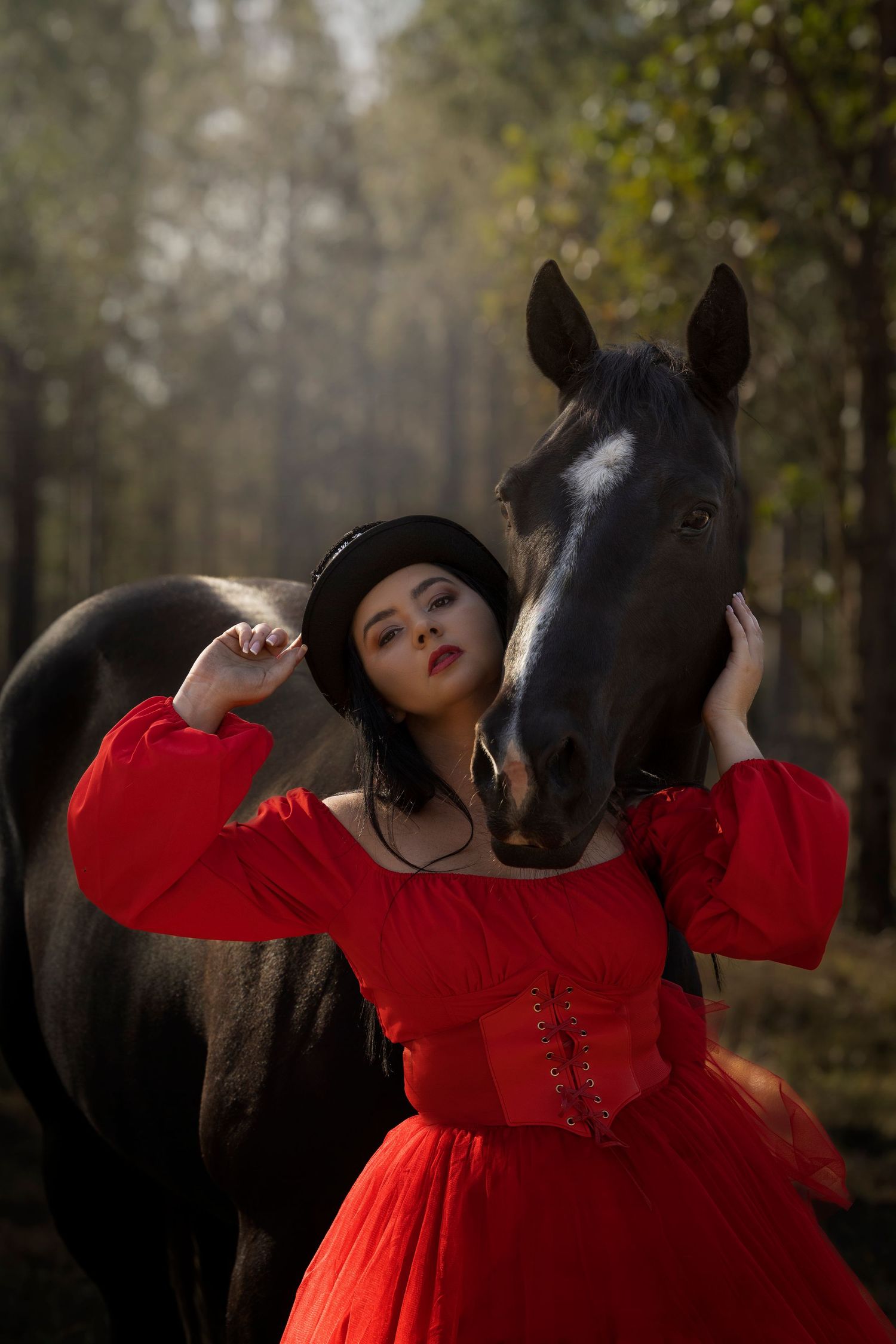 A striking portrait with a black horse and red vintage dress in a dreamy forest setting.