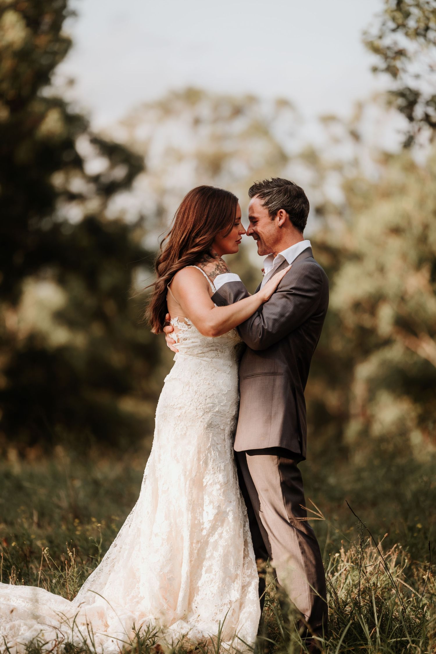 A romantic outdoor wedding moment captured at sunset with a couple embracing in formal attire amidst nature.