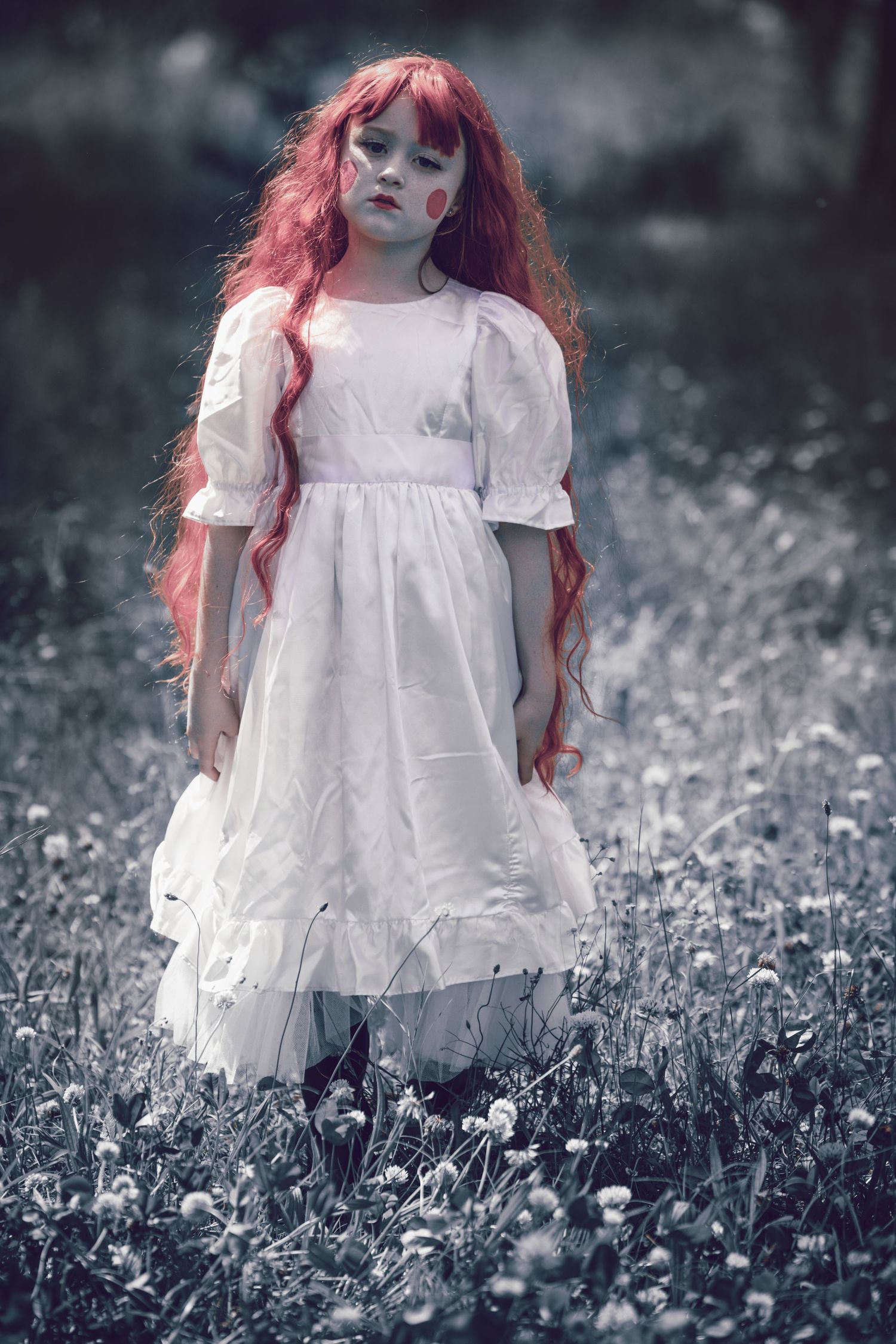 A doll wearing a white dress stands in a field of dandelions in a moody black and white scene with pink accents.