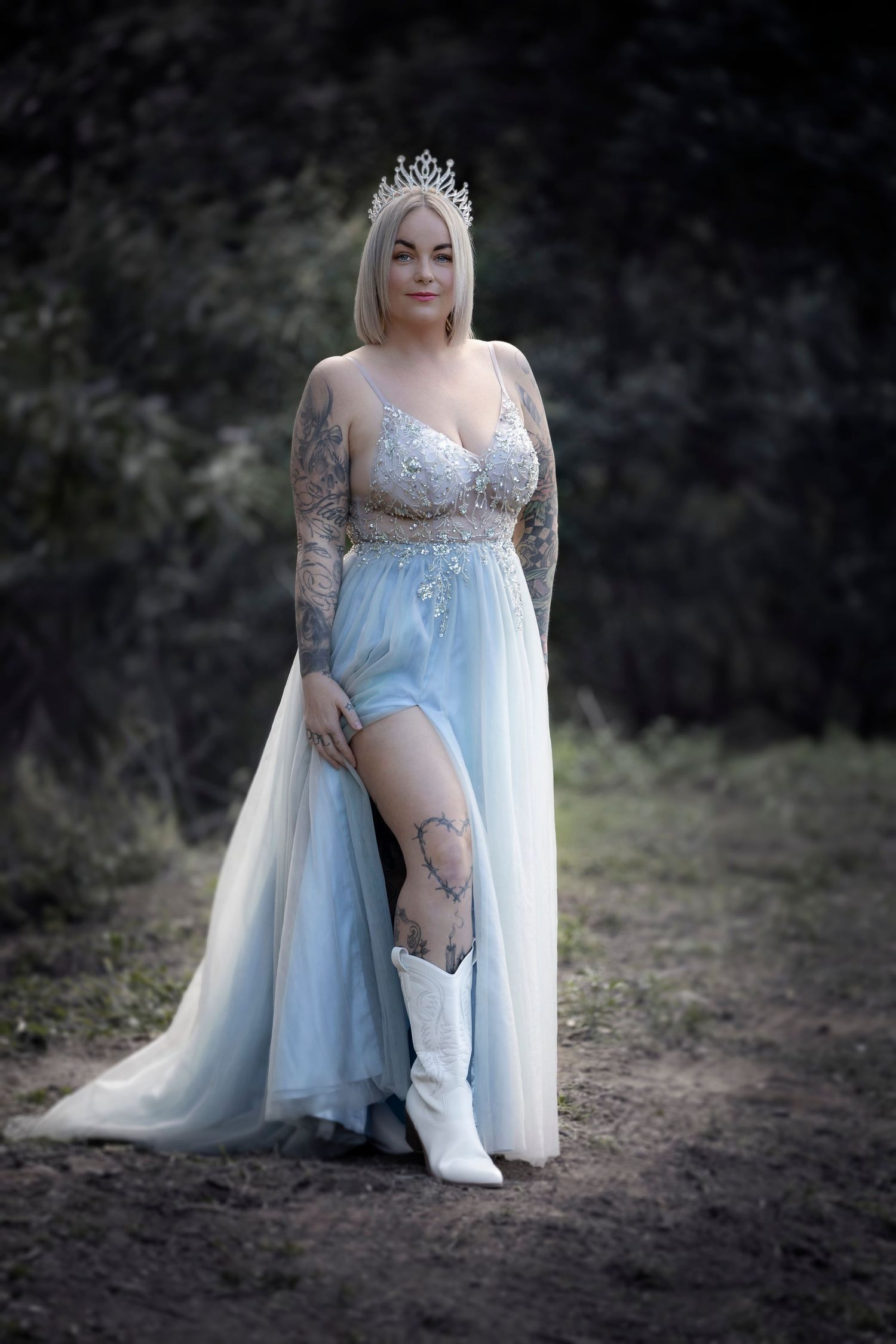 Ethereal figure in light blue gown and crown poses outdoors wearing white cowboy boots.
